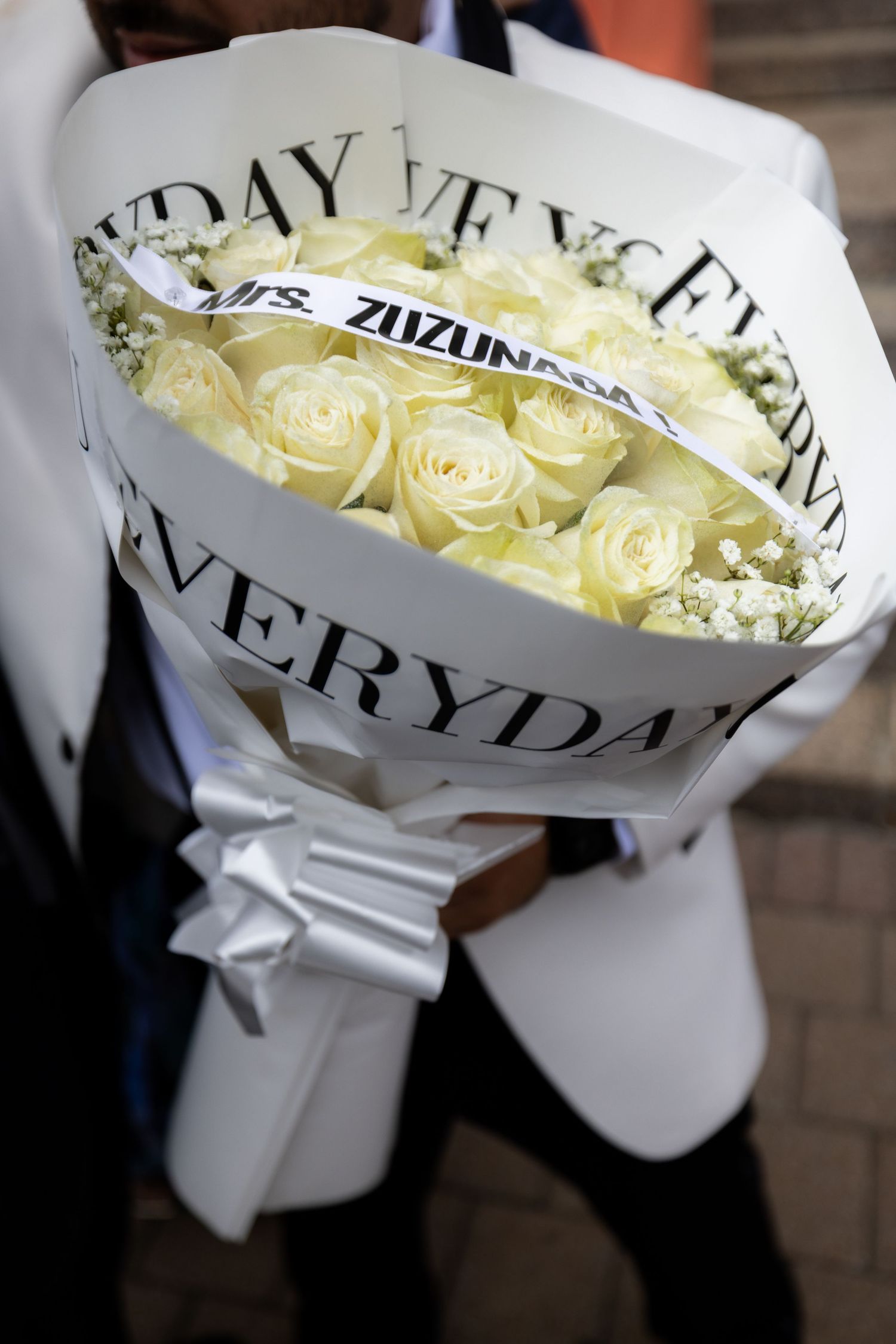 A bouquet of cream-colored roses wrapped in white paper with 'EVERYDAY' text and baby's breath accents.