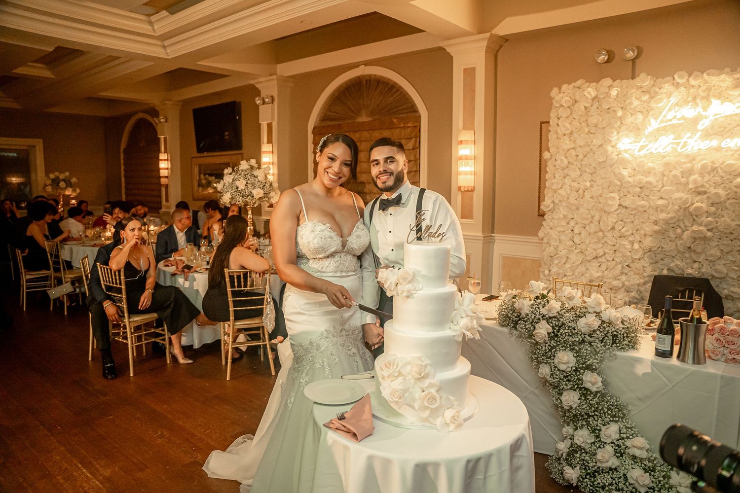 Elegant wedding celebration with a white multi-tiered cake and floral decorations in a luxurious ballroom setting.