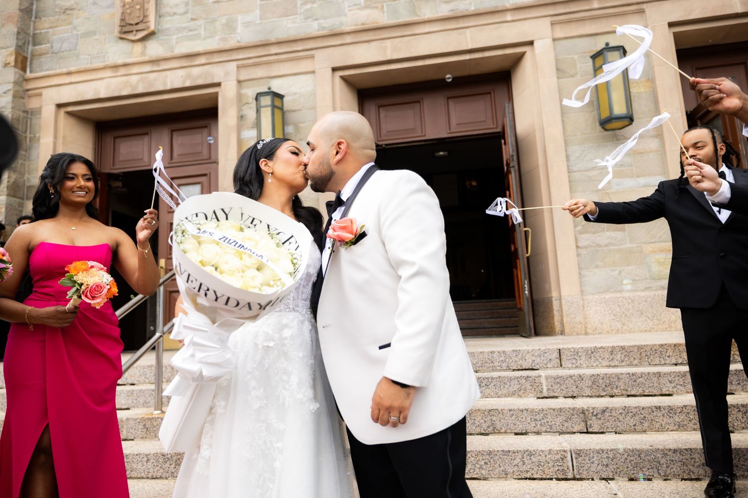 A joyful wedding celebration with multiple couples dancing and embracing on stone steps at an elegant venue.