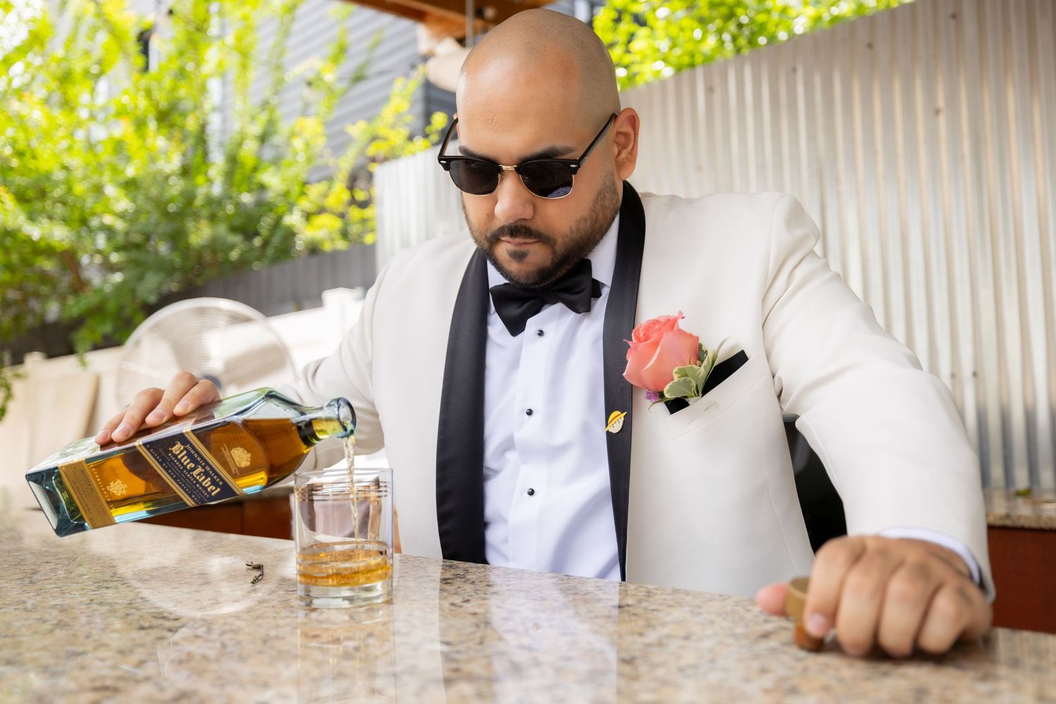 Groomsmen in formal attire share drinks and laughs at an outdoor wedding celebration.