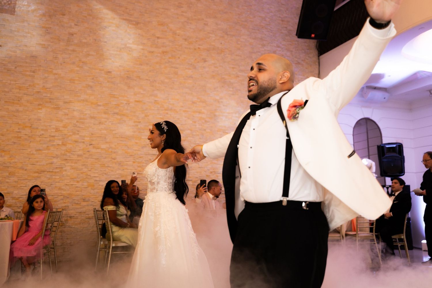 Wedding reception dance floor scene with flowing white dresses in motion under dim lighting.