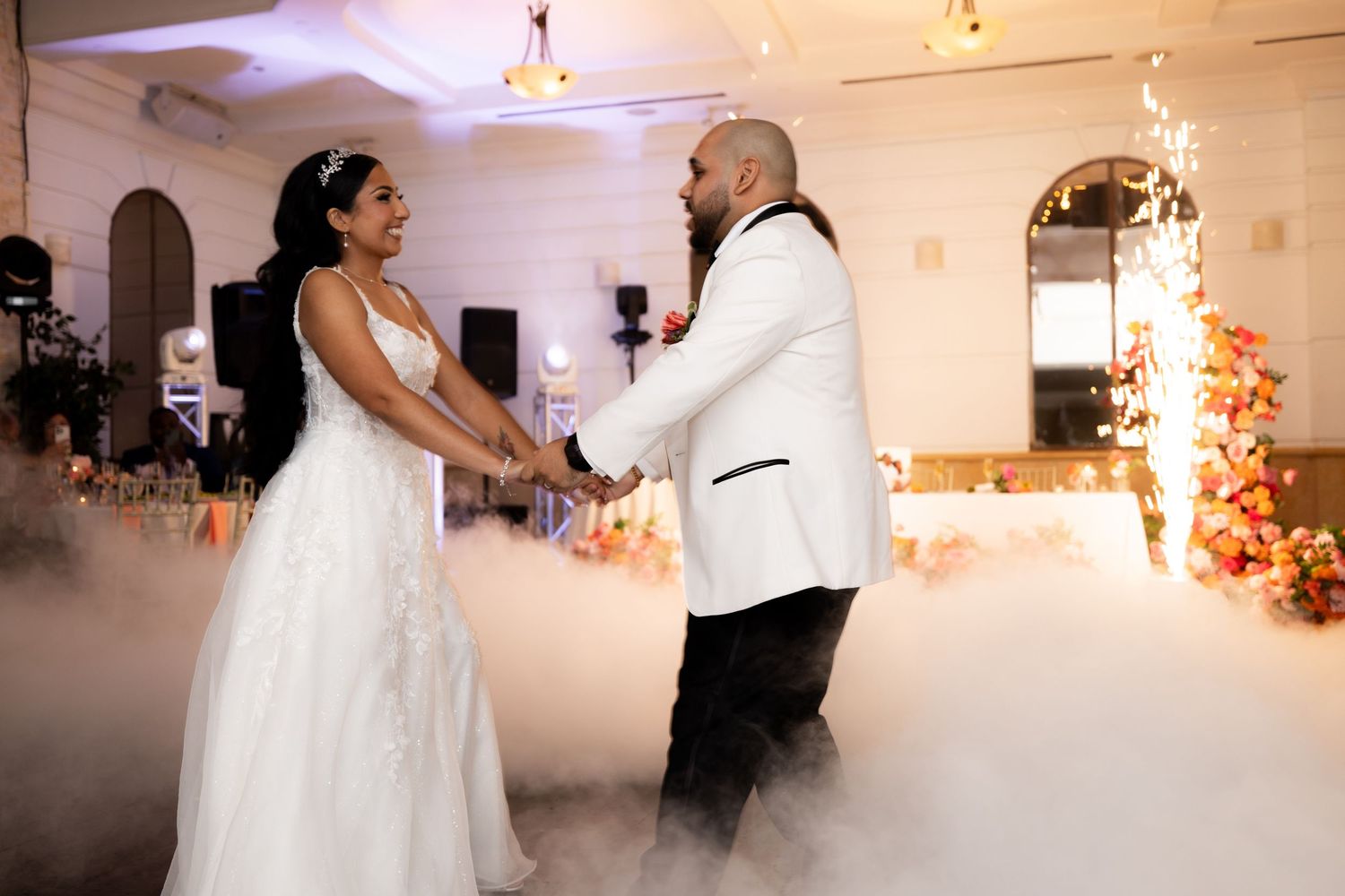 A couple shares their first dance as newlyweds on a misty dance floor with romantic lighting and floral decor.