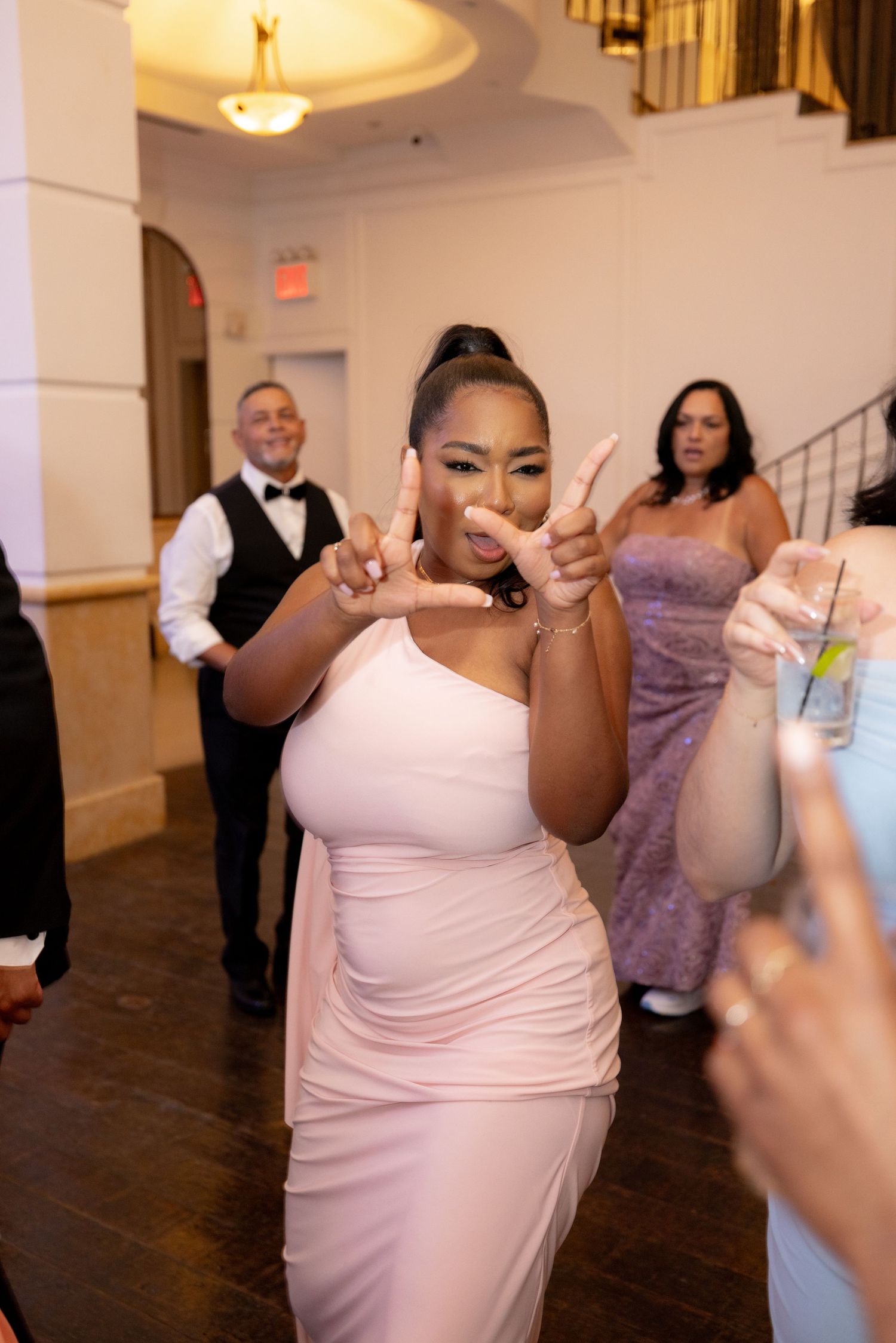 Wedding guest dances enthusiastically on wooden dance floor in pink dress during reception celebration.