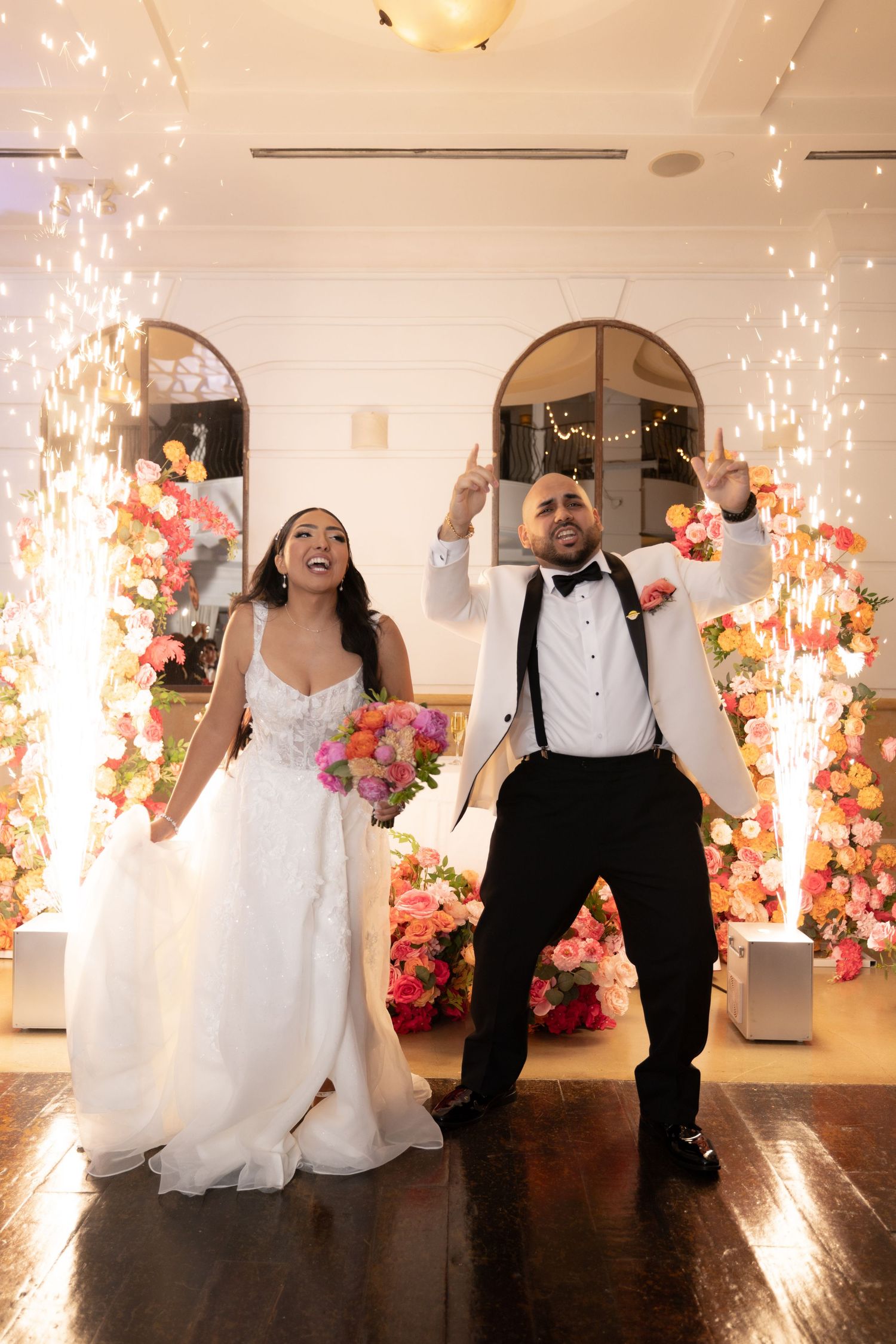 Wedding celebration with sparklers and floral decorations in an elegant white indoor venue.