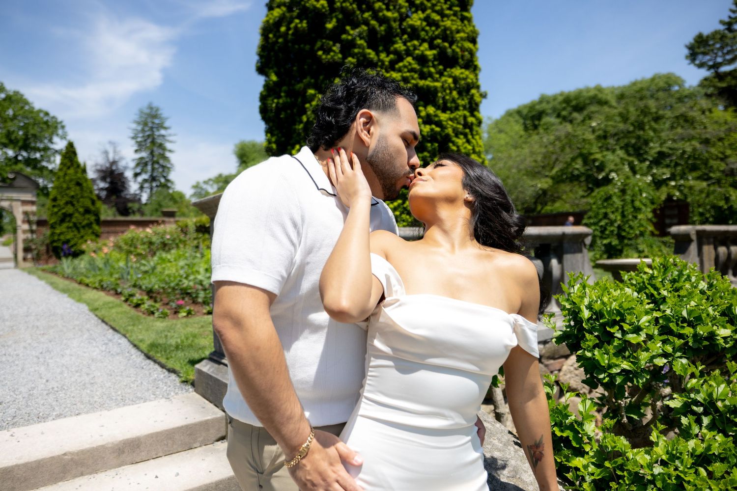 A couple shares a romantic moment in a lush green garden setting on a sunny day.