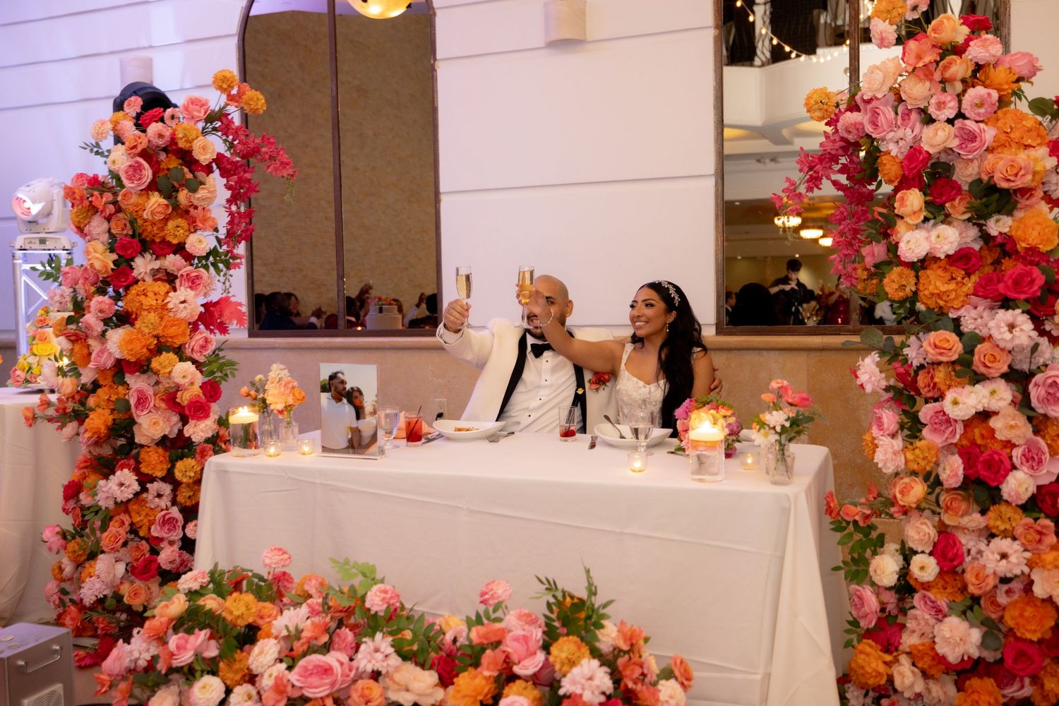 Elegant wedding reception setup with vibrant pink and orange floral arrangements on white-clothed tables.