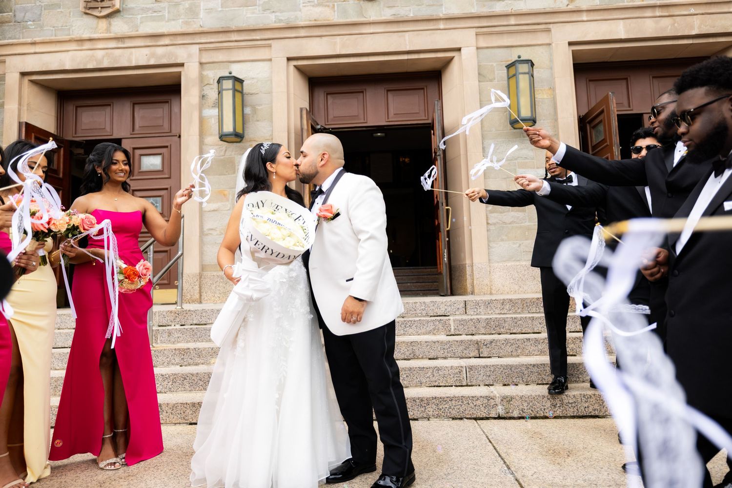 Guests throw white flower petals during an outdoor wedding celebration at a historic stone venue.