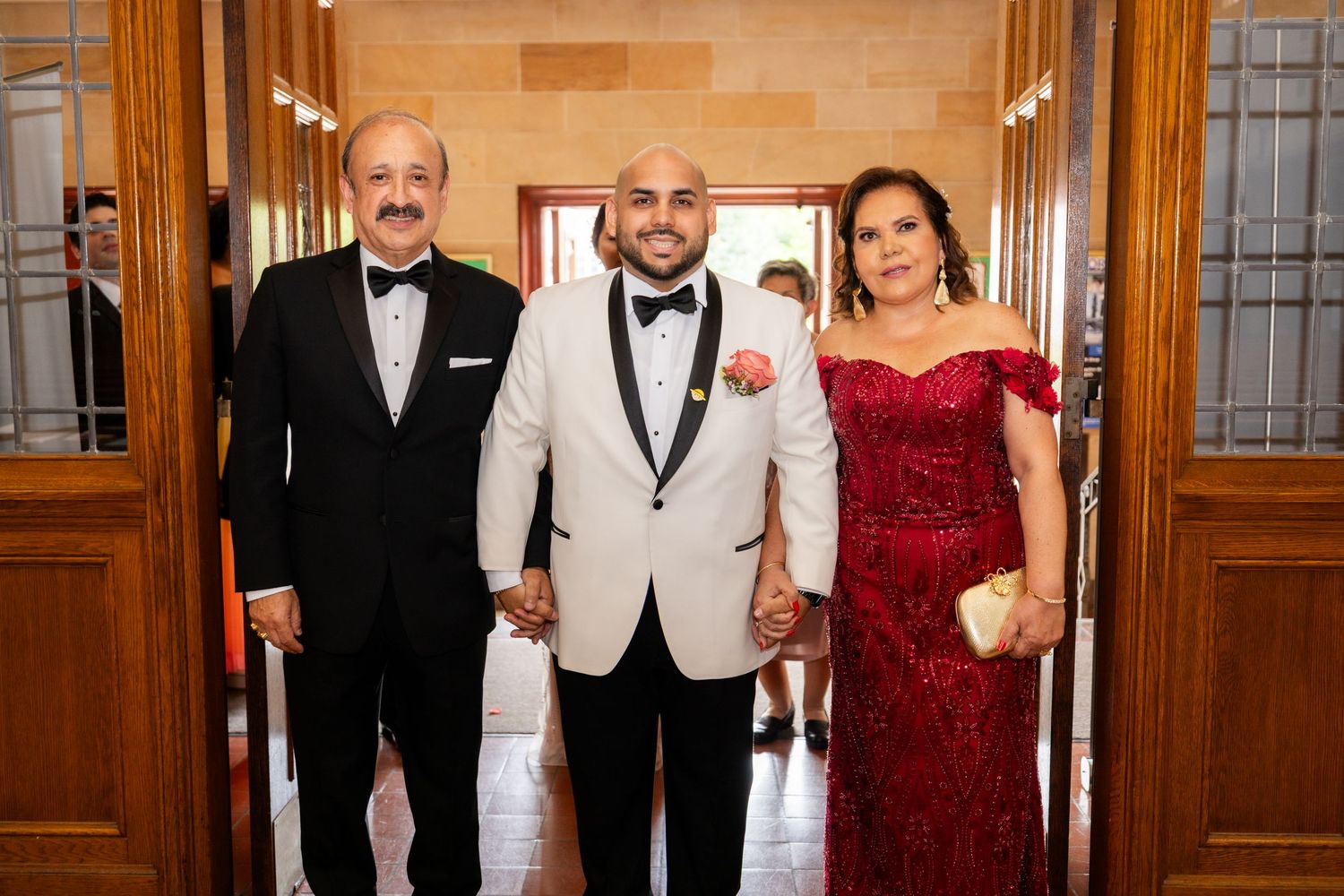 Wedding guests in formal attire dancing and celebrating at an elegant indoor reception venue with wooden paneled walls.
