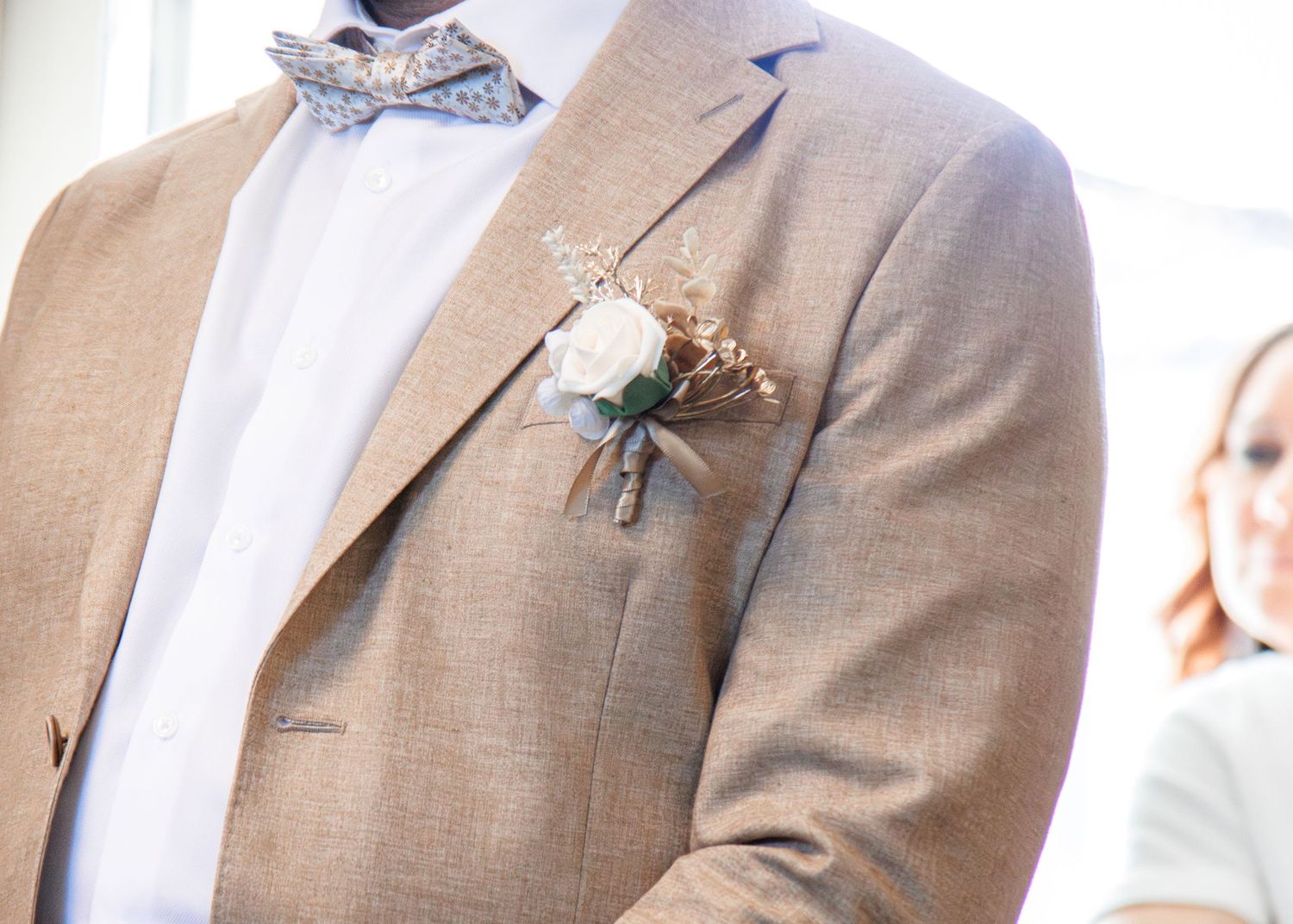 A person wearing a beige suit jacket with a white shirt against a light background.
