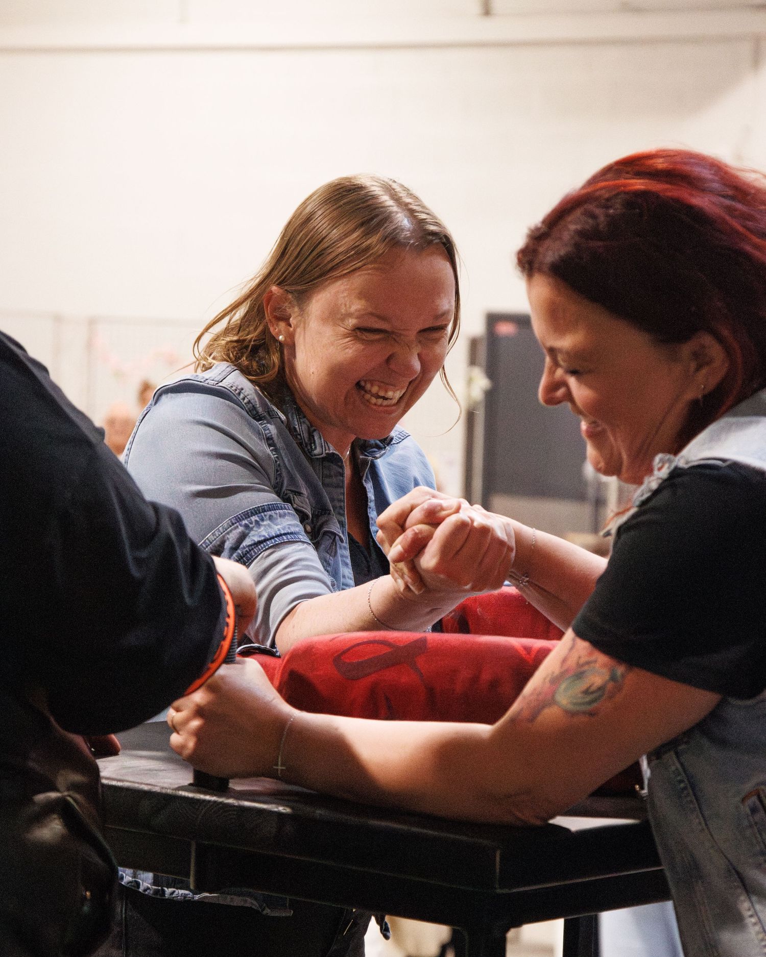 Two competitors engaged in intense arm wrestling match at indoor venue.