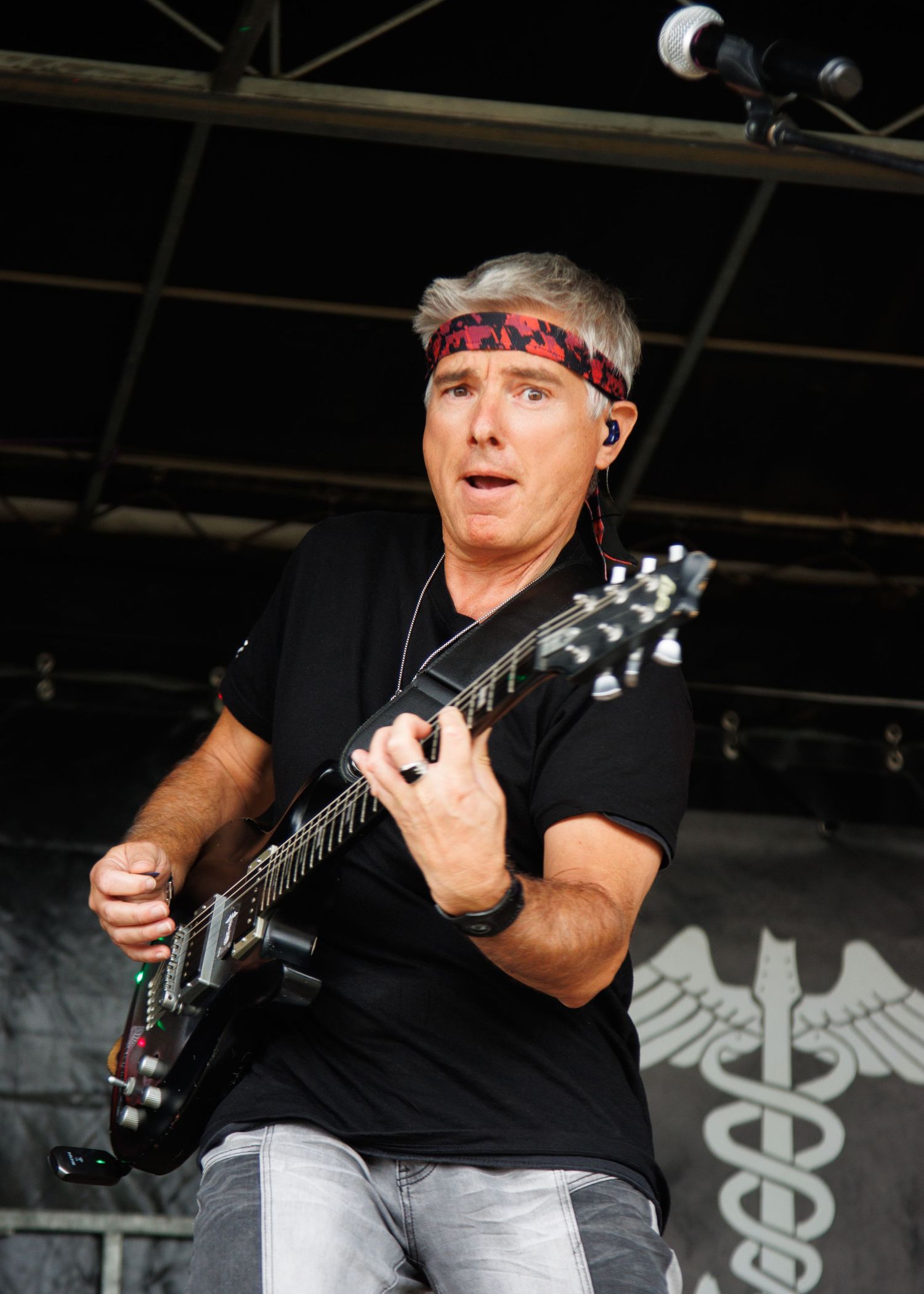 Musician in black attire playing electric guitar on stage with lighting effects.