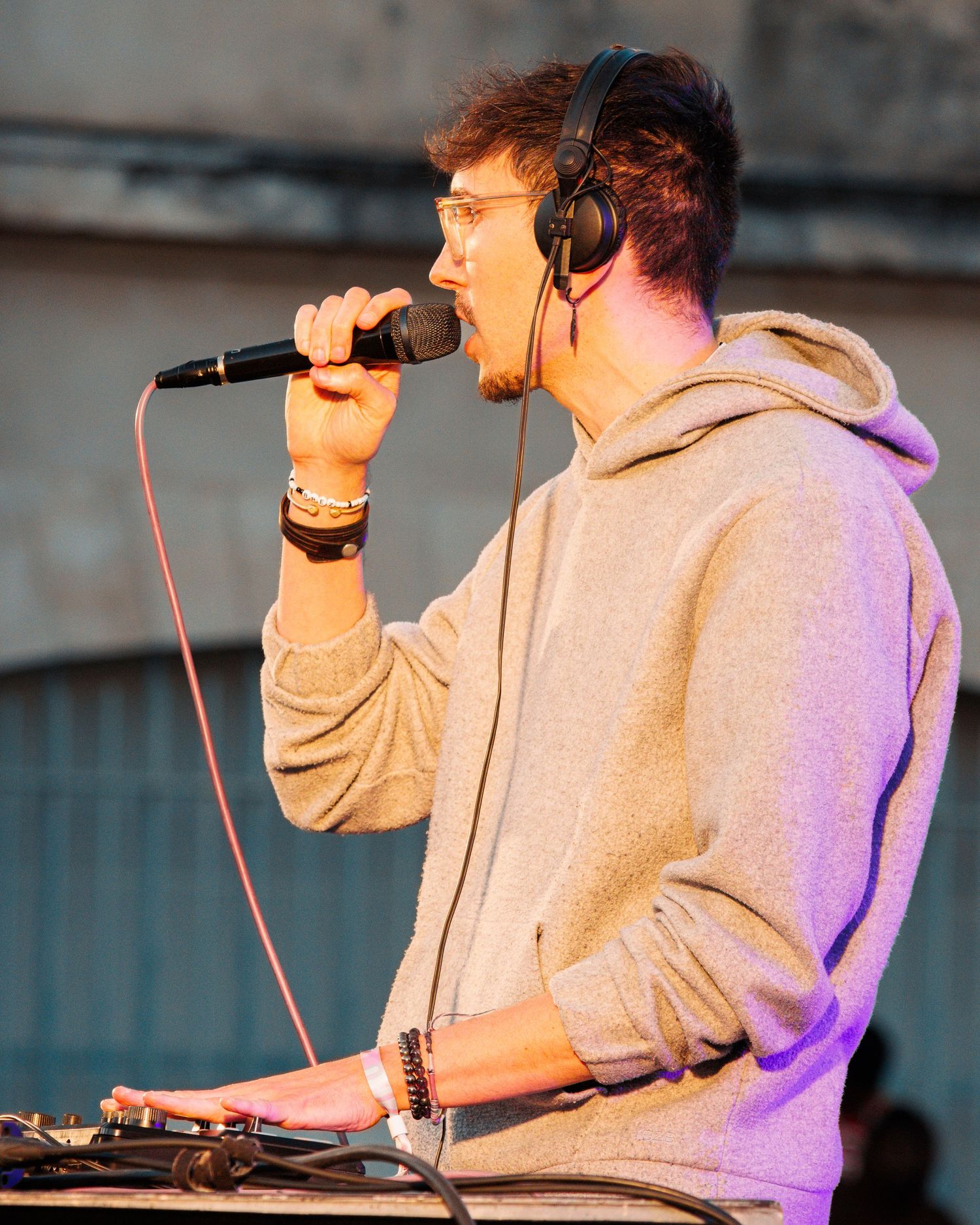 Performer in grey hoodie using audio equipment while singing.