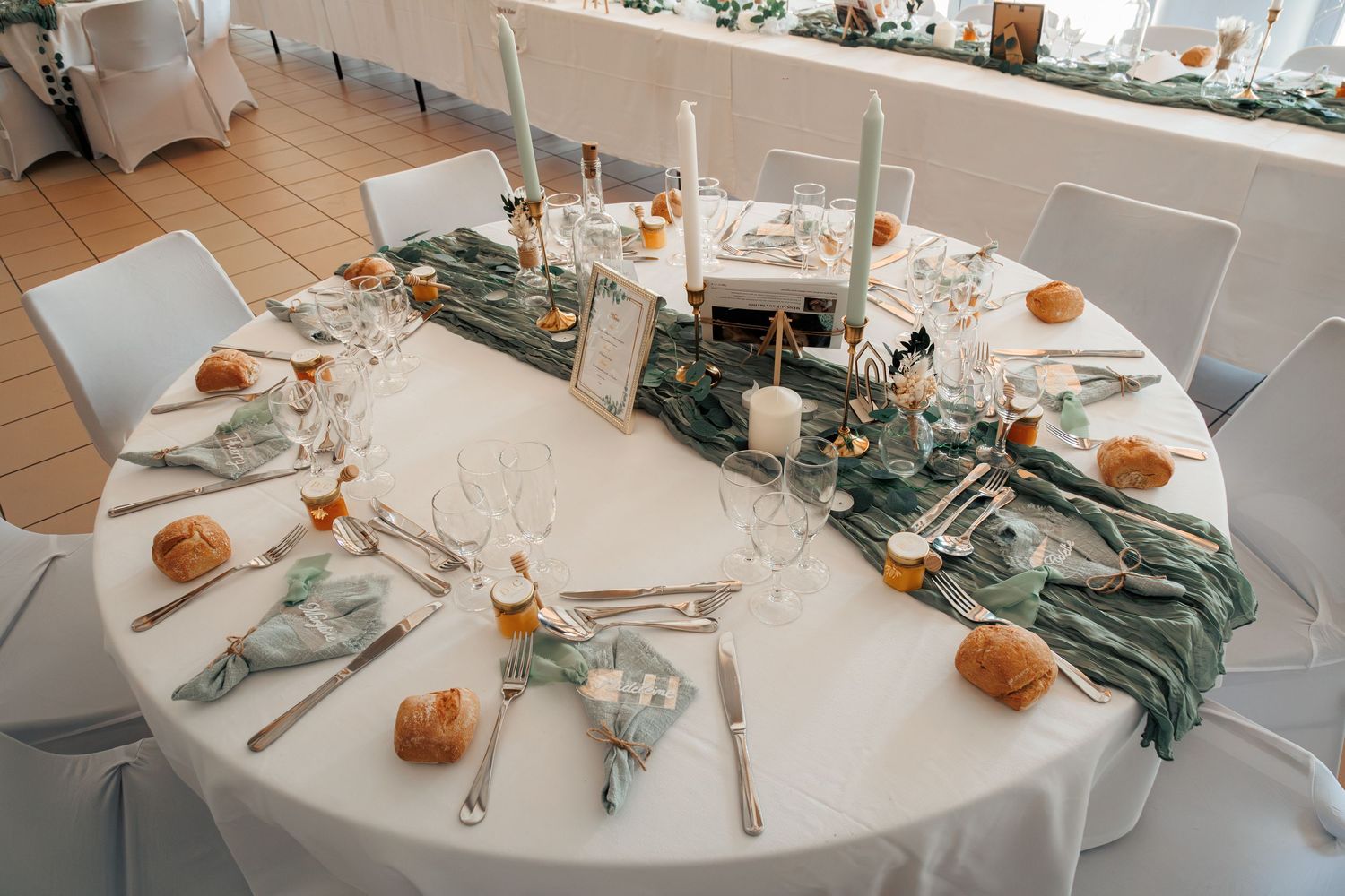 Elegant round wedding table with sage green runner and orange decor.