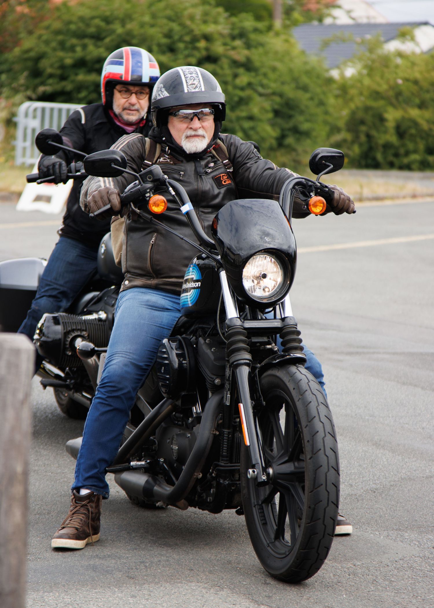 Two motorcyclists in helmets riding a black motorcycle on a road with autumn trees.