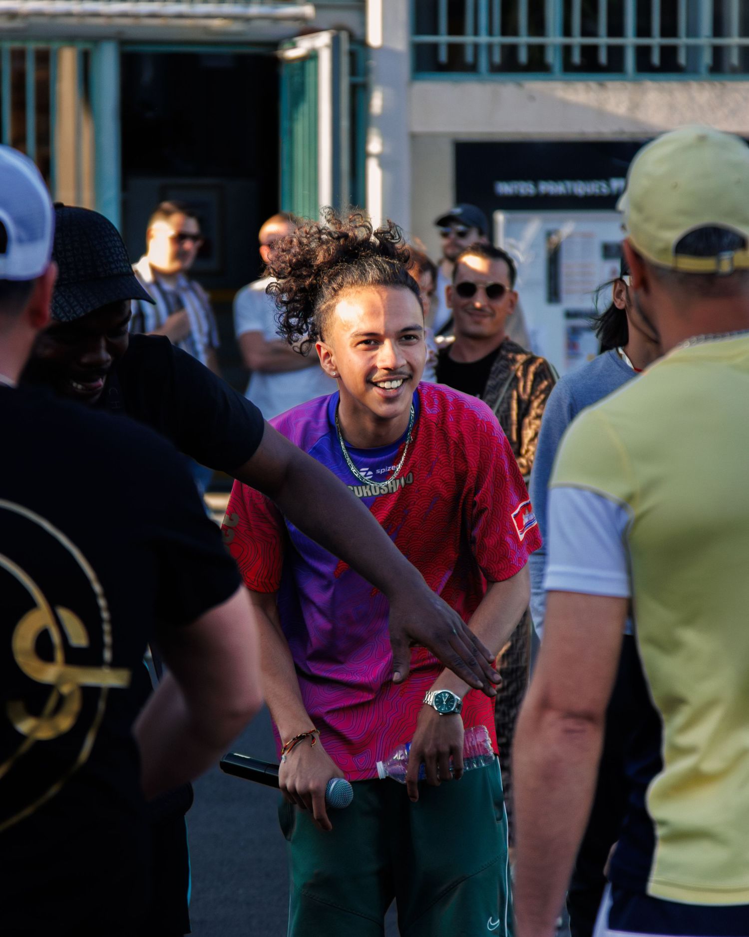 Person in bright pink shirt smiles and interacts with others at outdoor event.
