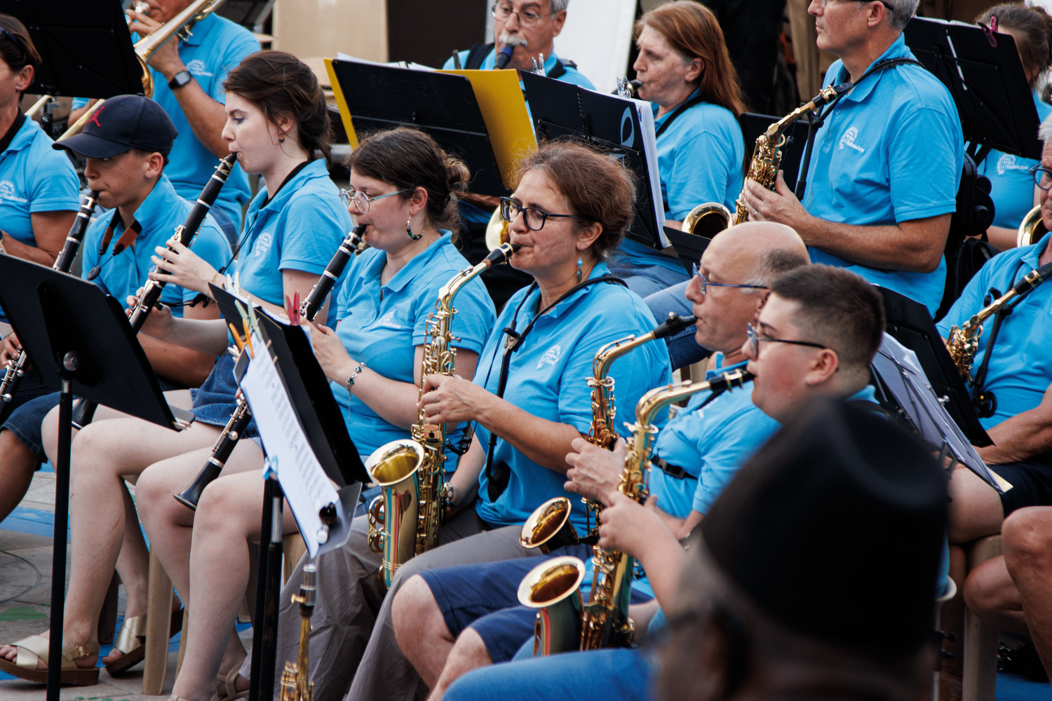 Musicians in blue uniforms play saxophones during an outdoor concert performance.