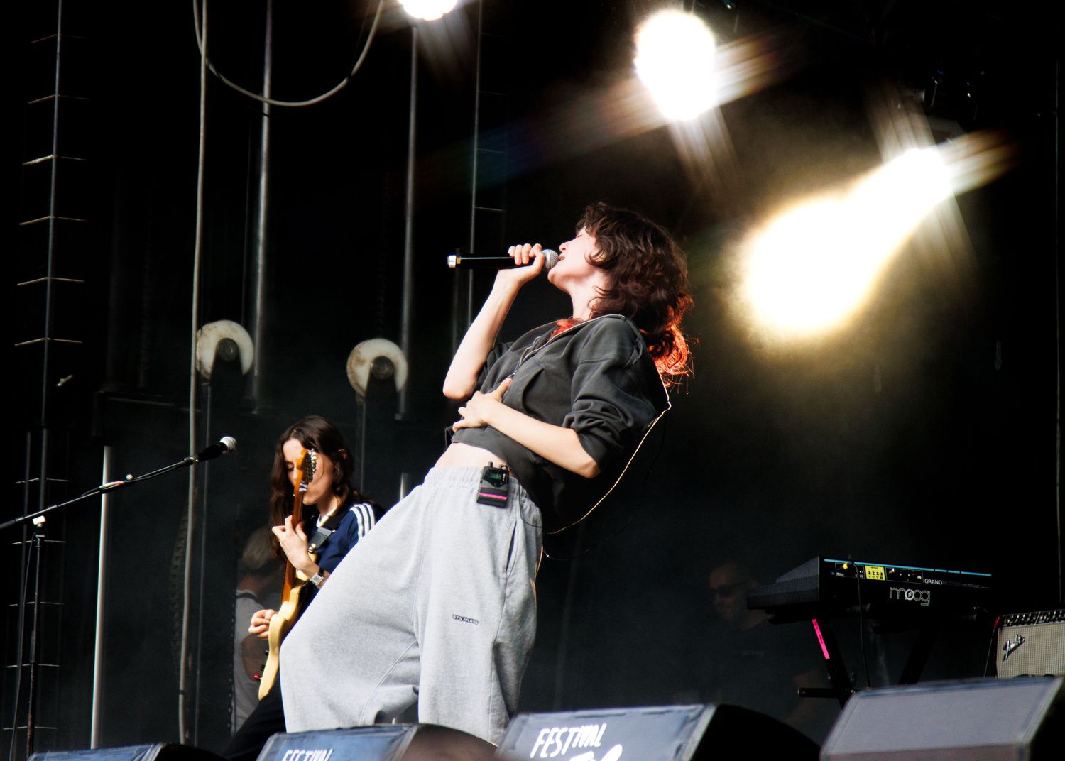 Concert performer on stage energetically singing into microphone with dramatic stage lighting.