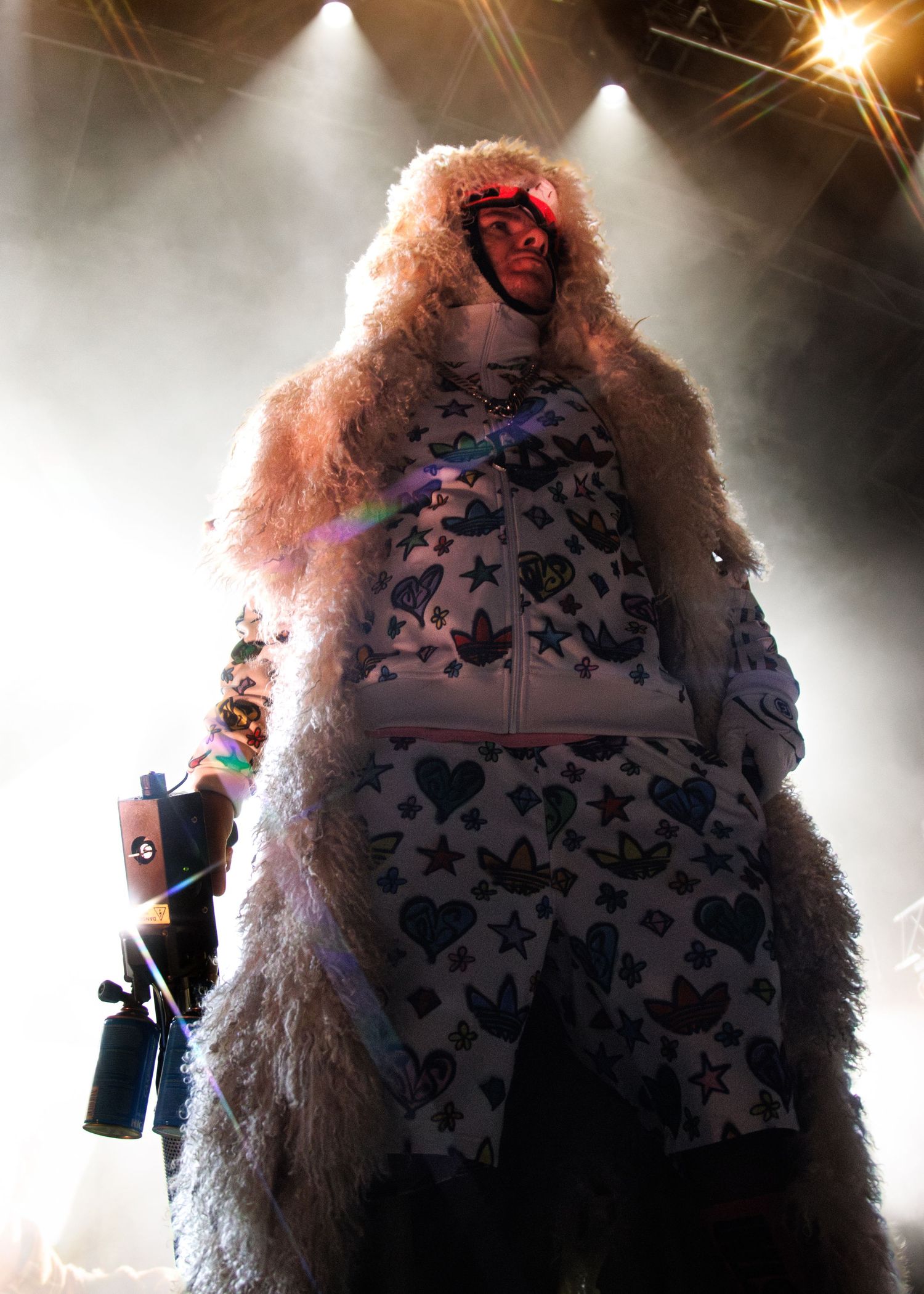 A performer in a furry pink costume and patterned outfit stands on stage amid dramatic concert lighting.