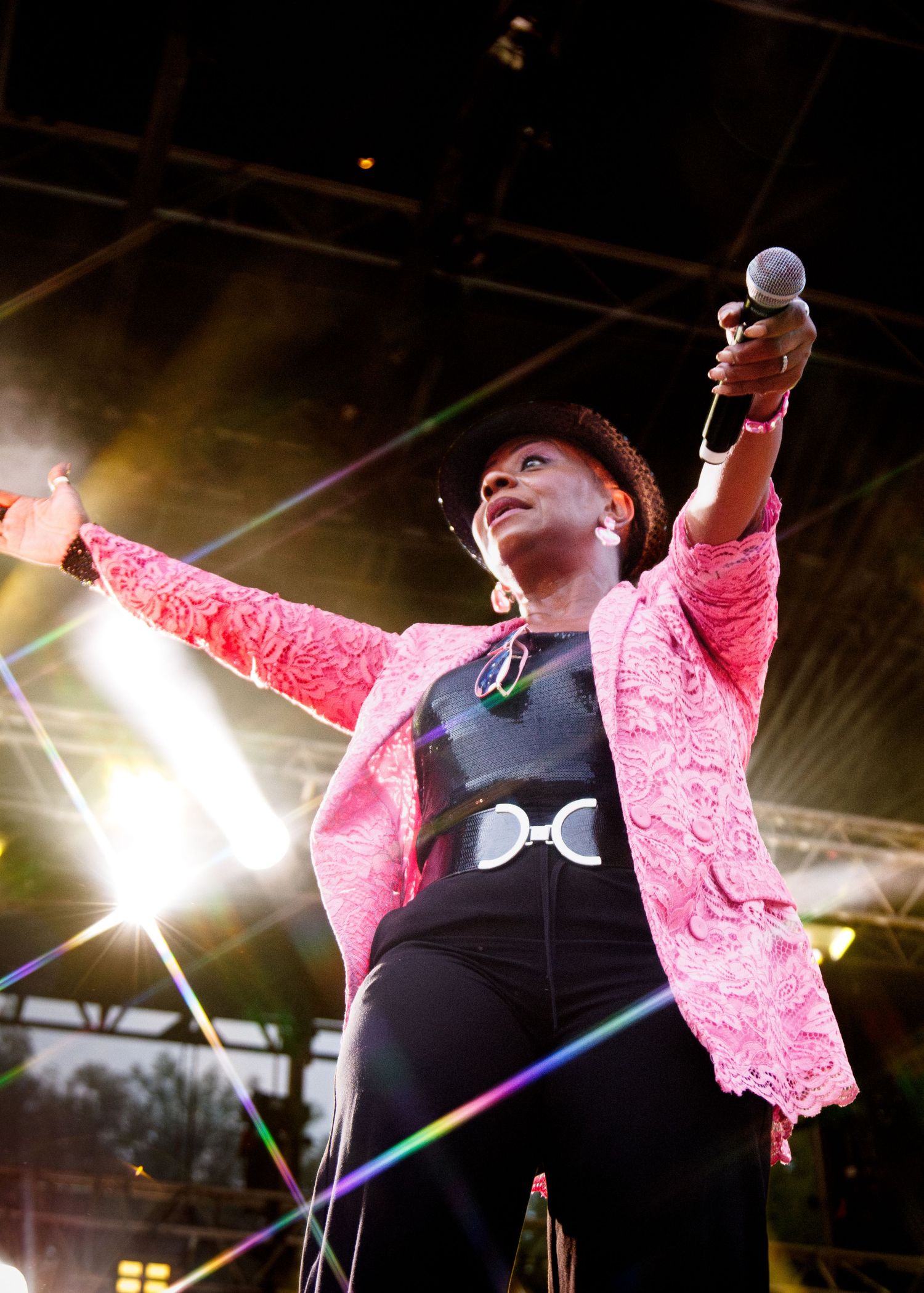 Energetic performer in a pink sequined jacket and black outfit sings passionately on stage under dramatic lighting.