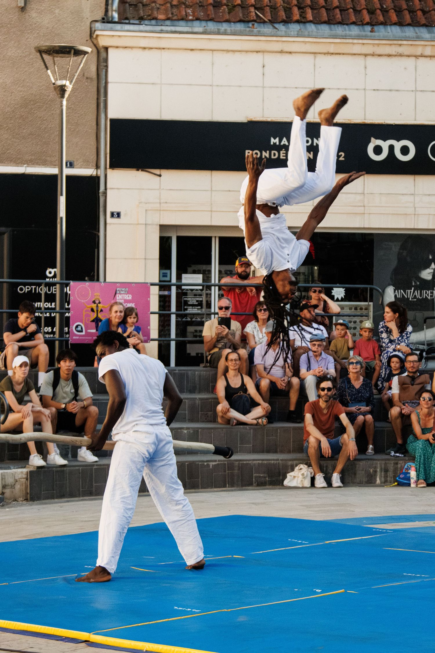 Street performers execute an upside-down acrobatic stunt in front of an engaged audience.