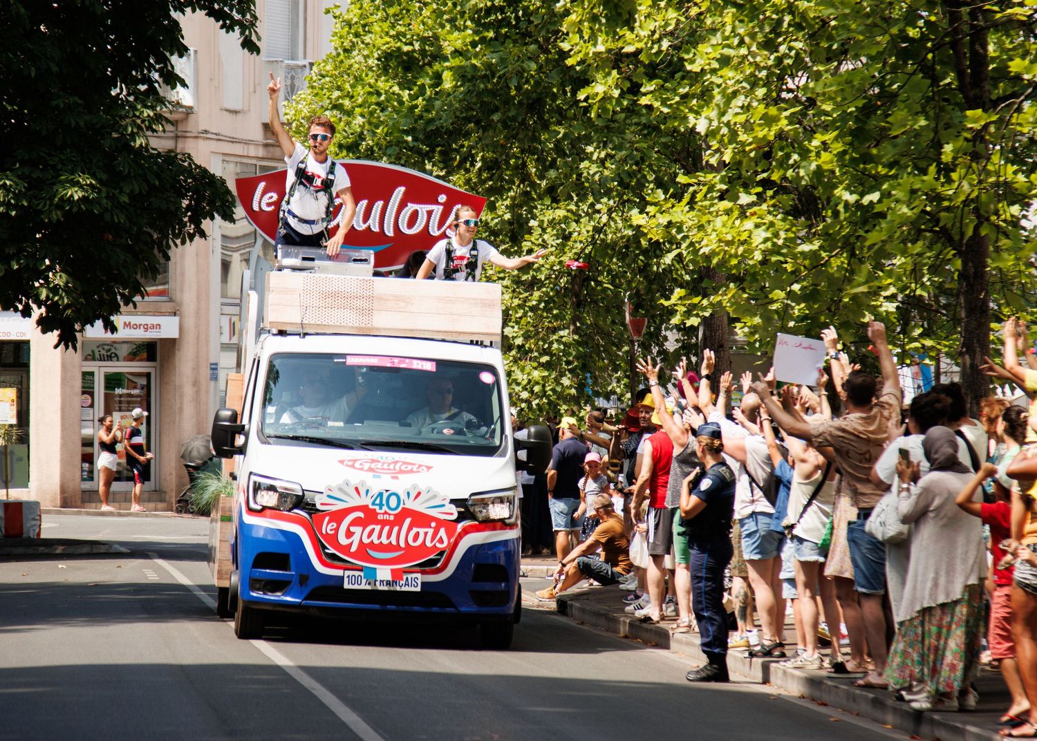 A Galafop branded promotional vehicle drives past crowds of spectators on a tree-lined street.