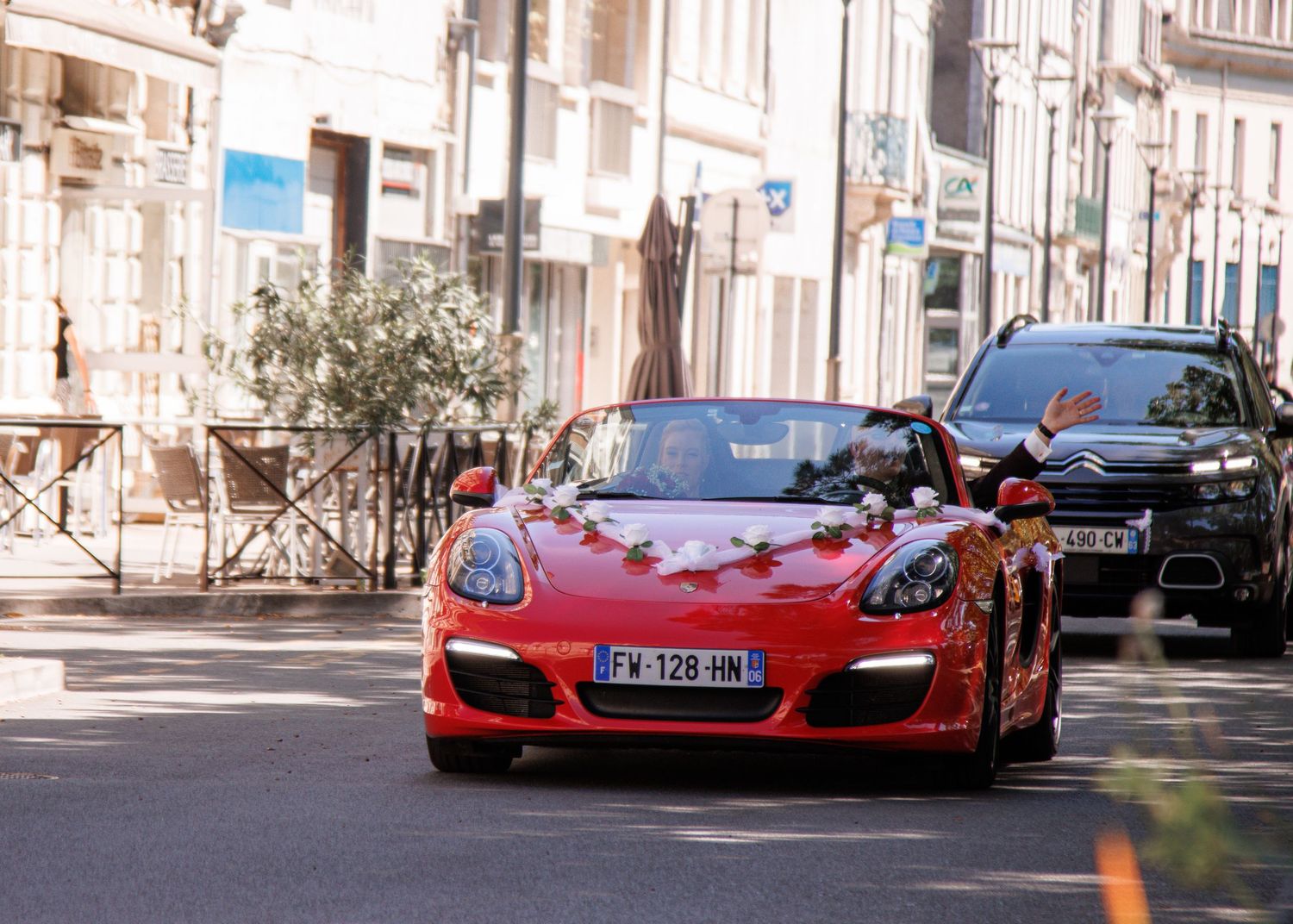 A red Porsche Boxster convertible decorated for a wedding drives through a French town street.