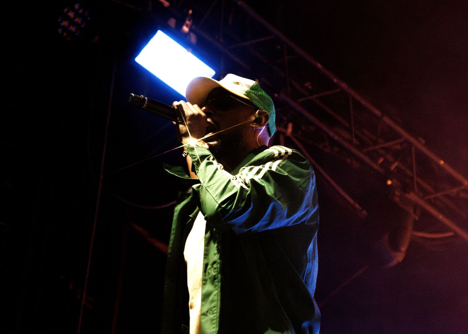 Concert performer on dark stage illuminated by blue spotlight during energetic live music performance.