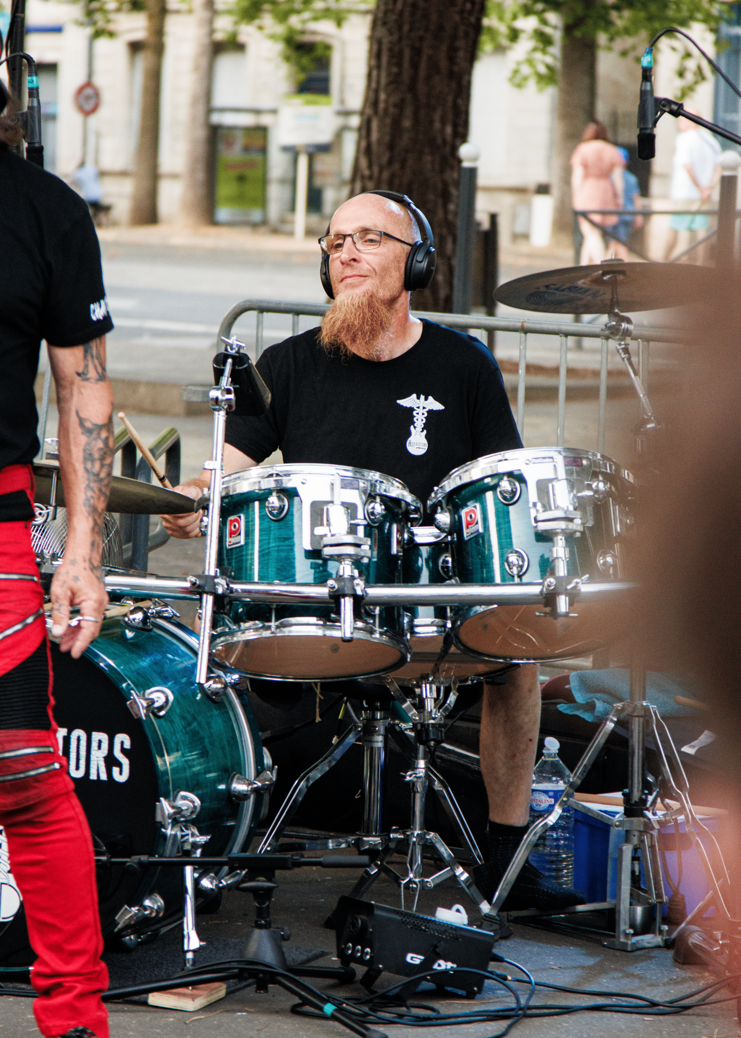 Bearded drummer performs with teal drum kit at outdoor venue.