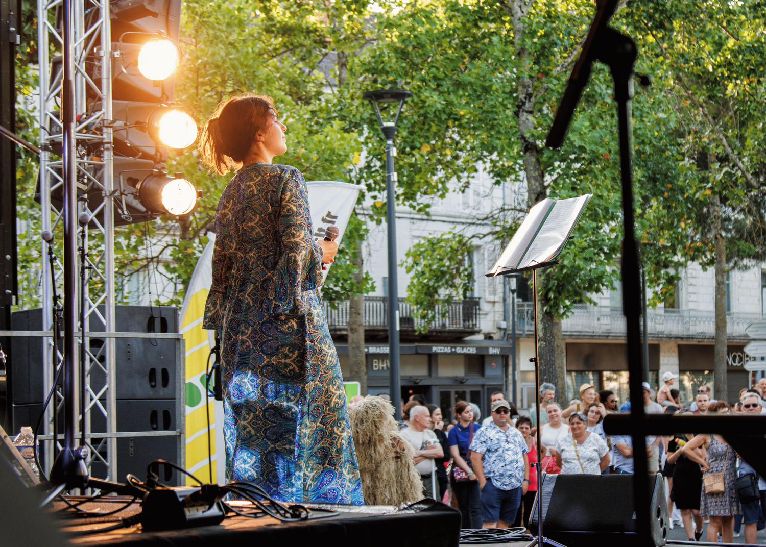 Stage lighting and sound equipment set up against a backdrop of green trees.