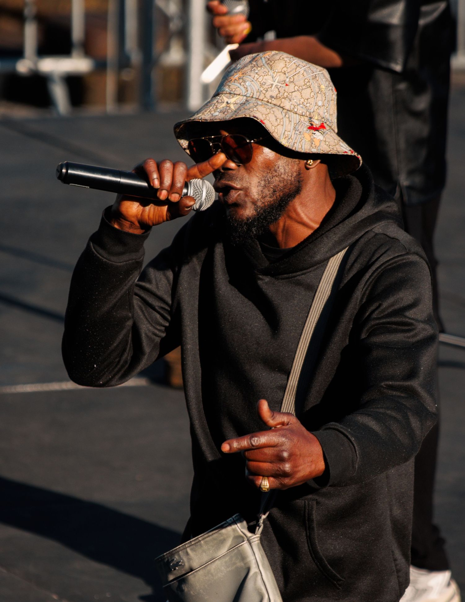 Artist performing with microphone wearing patterned bucket hat and black hoodie.