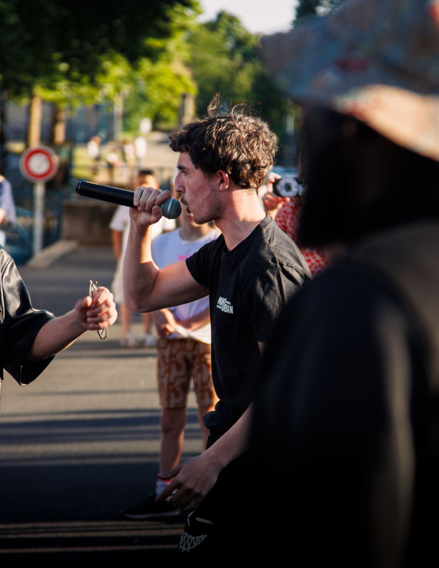 Artist in black t-shirt performs with microphone at outdoor summer event.