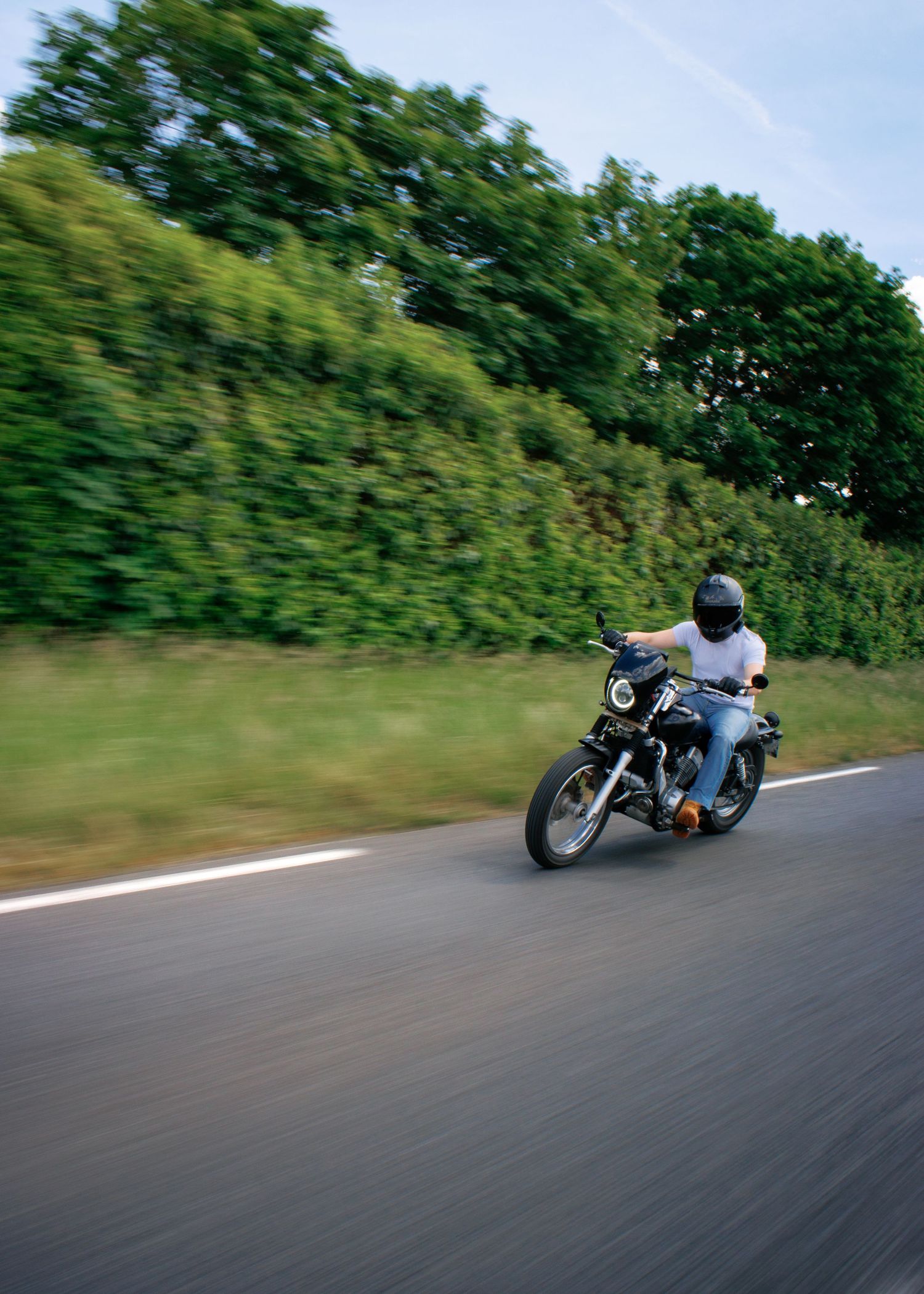 Motorcyclist riding on a country road surrounded by lush green hedges, captured with motion blur effect.