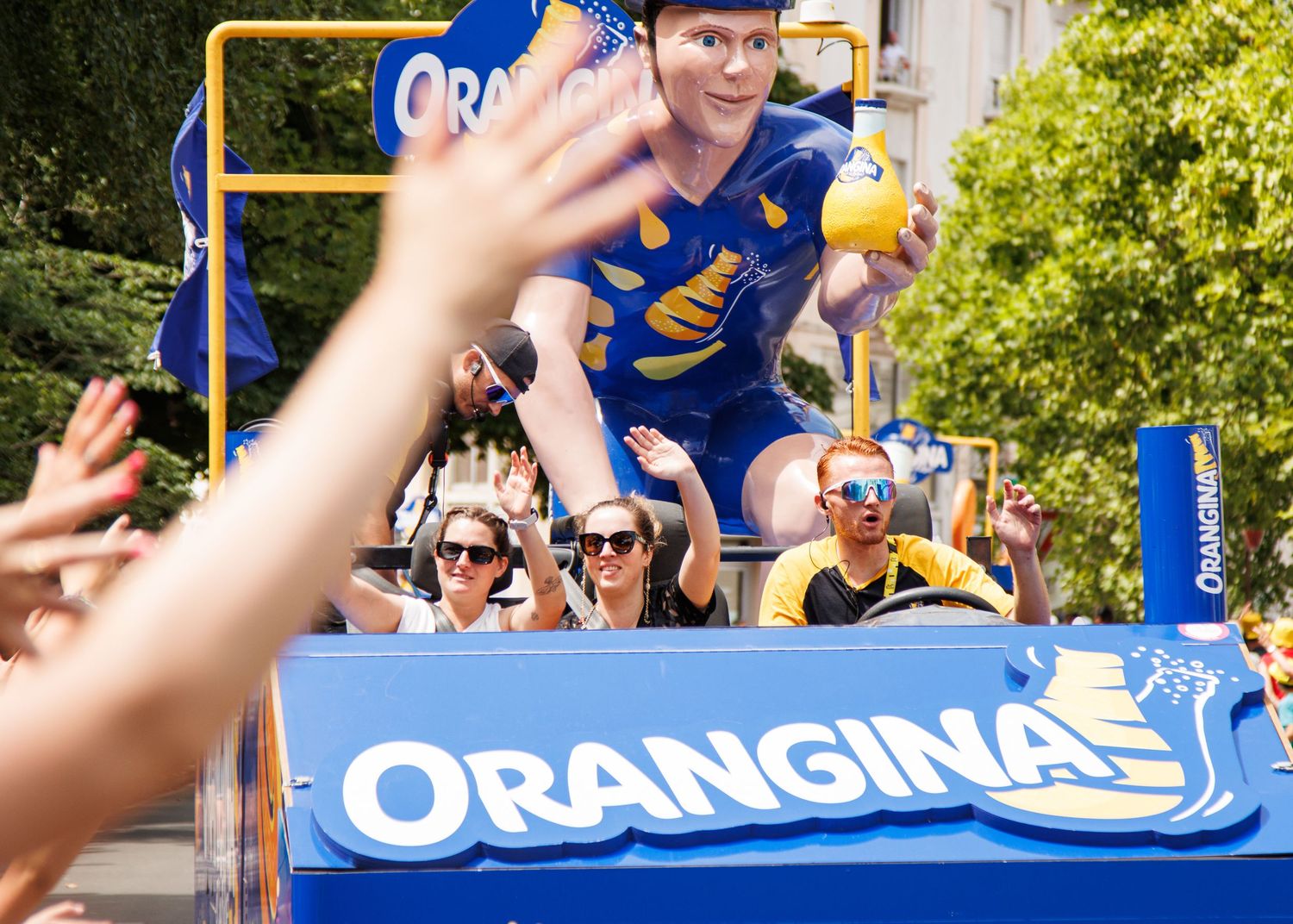 A promotional vehicle for Orangina with crowds of spectators waving along the street.
