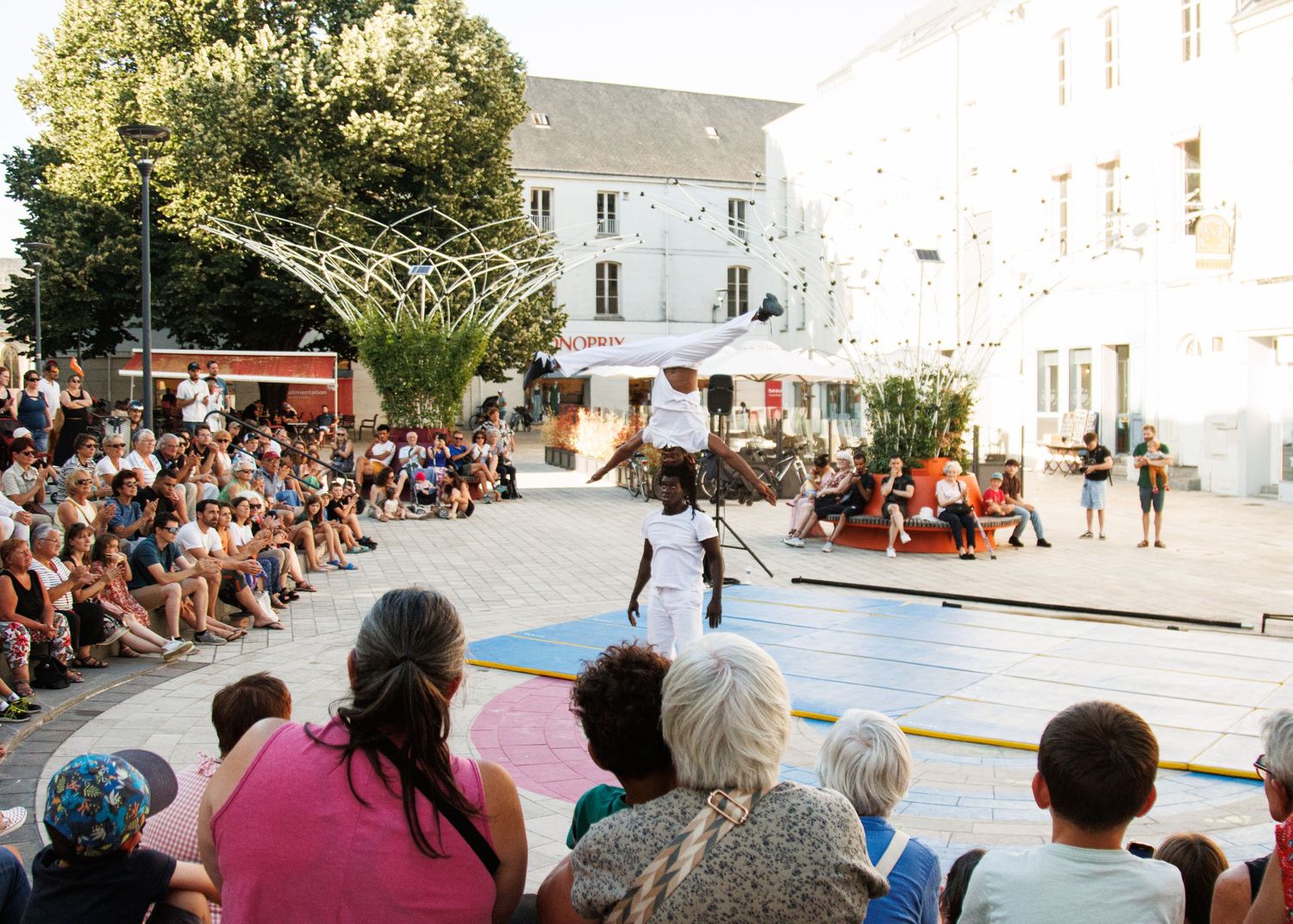 Acrobatic performance on colorful mat entertains large outdoor crowd in European plaza.