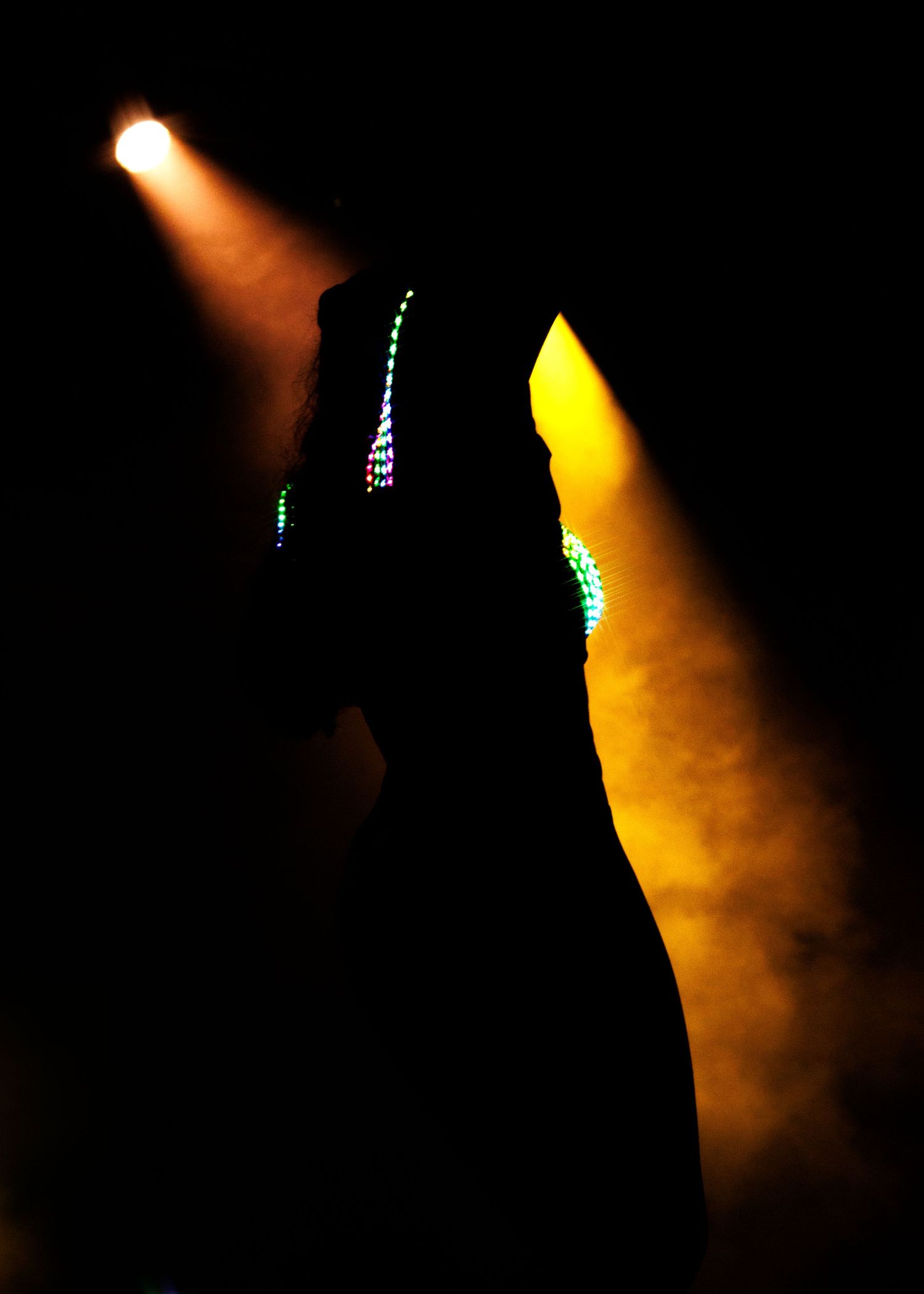 Silhouetted figure performing on stage with dramatic orange and yellow spotlights creating a moody atmosphere.