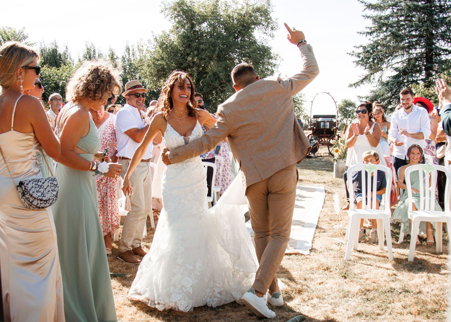 Newlyweds celebrate and dance with guests at an outdoor summer wedding reception in a rustic setting.