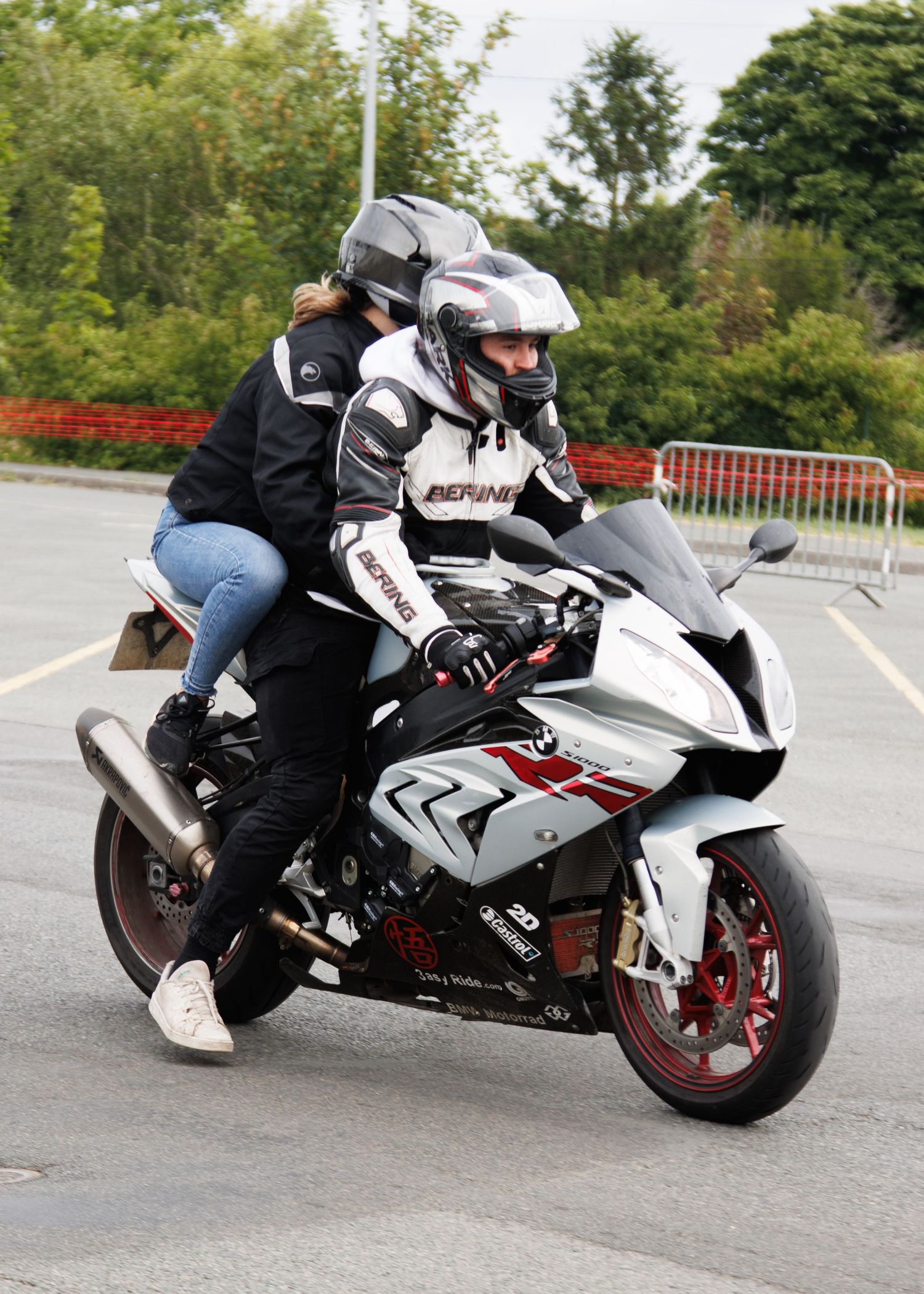 Motorcyclists riding a white sports bike on a curved road surrounded by greenery.