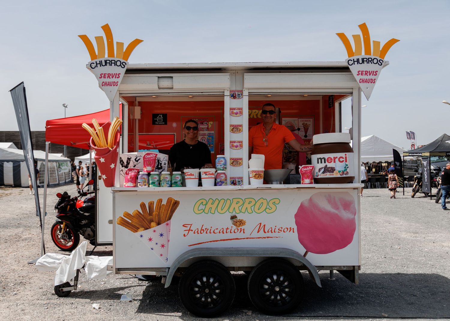 A churros food trailer vendor with two staff members serving fresh homemade churros at an outdoor event or market.