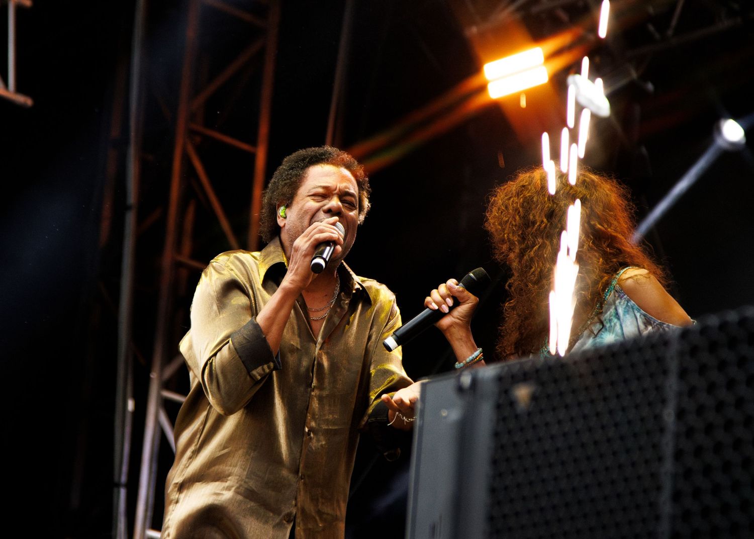 A passionate performer sings on stage during a concert with dramatic lighting and equipment visible in the background.