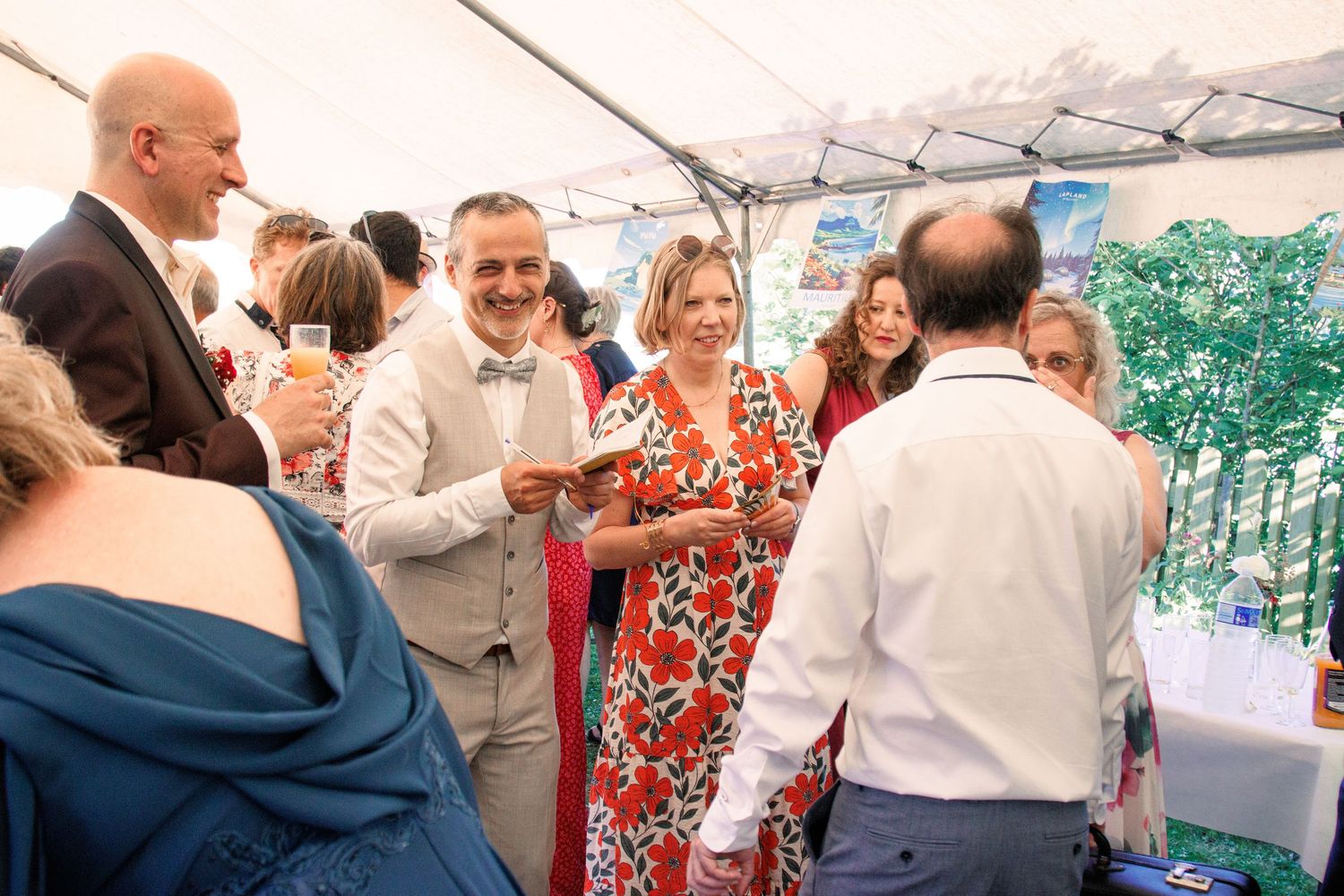 Wedding guests mingling and socializing under decorated tent at elegant outdoor wedding reception.