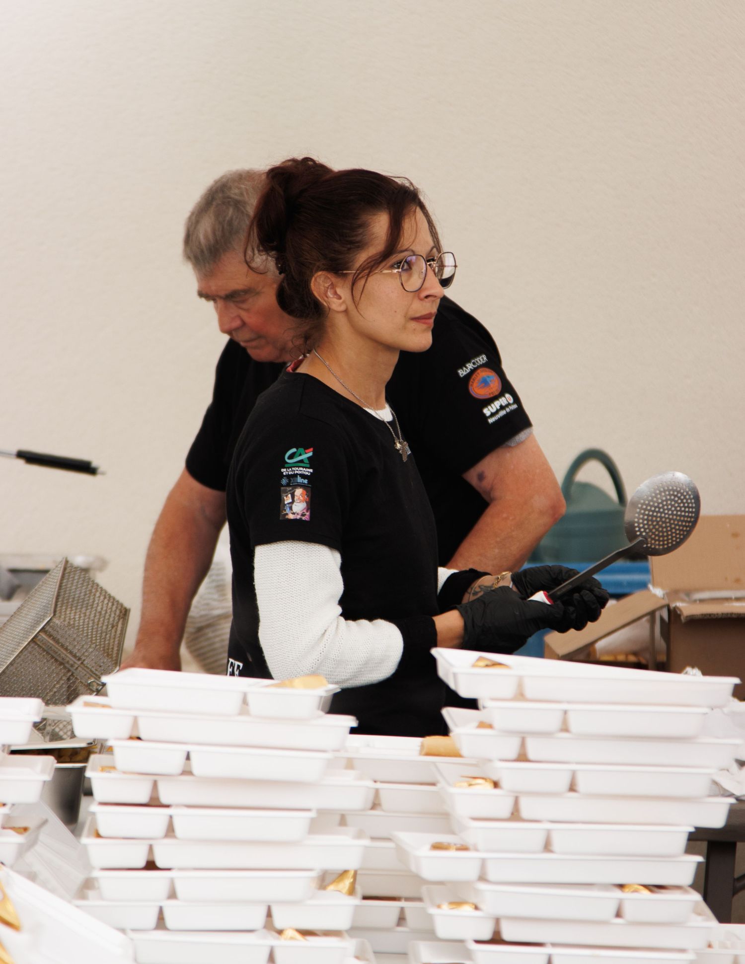 People in black shirts working at tables with stacks of white paper materials.