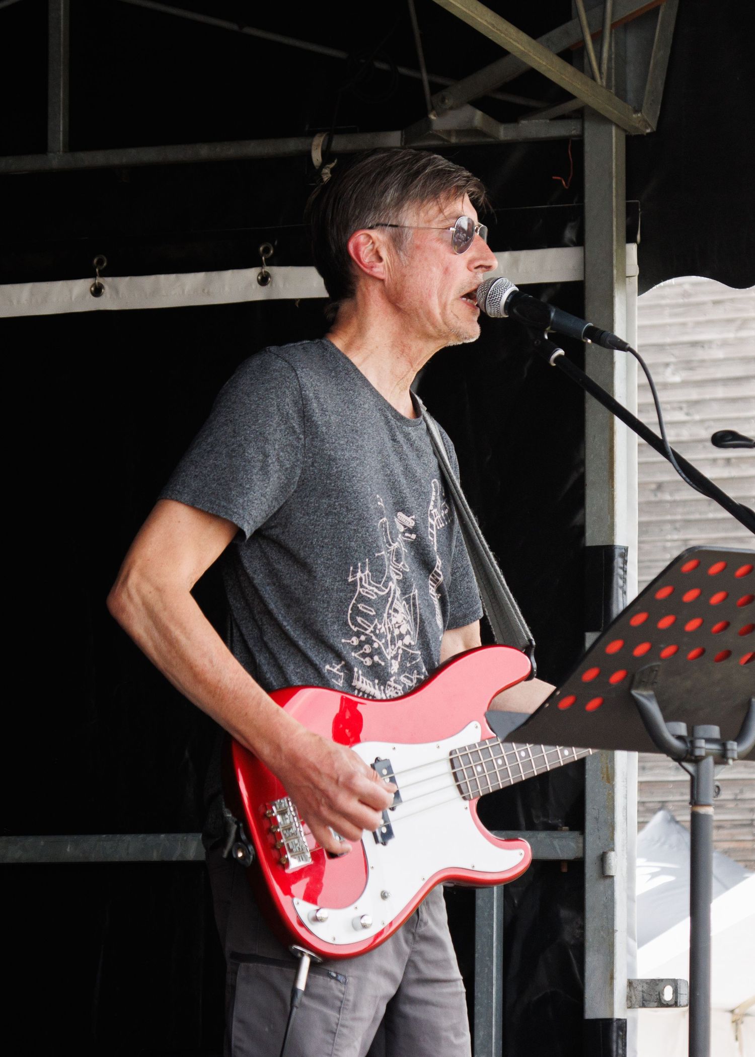 Musician in sunglasses performs on stage with a red and white electric guitar.