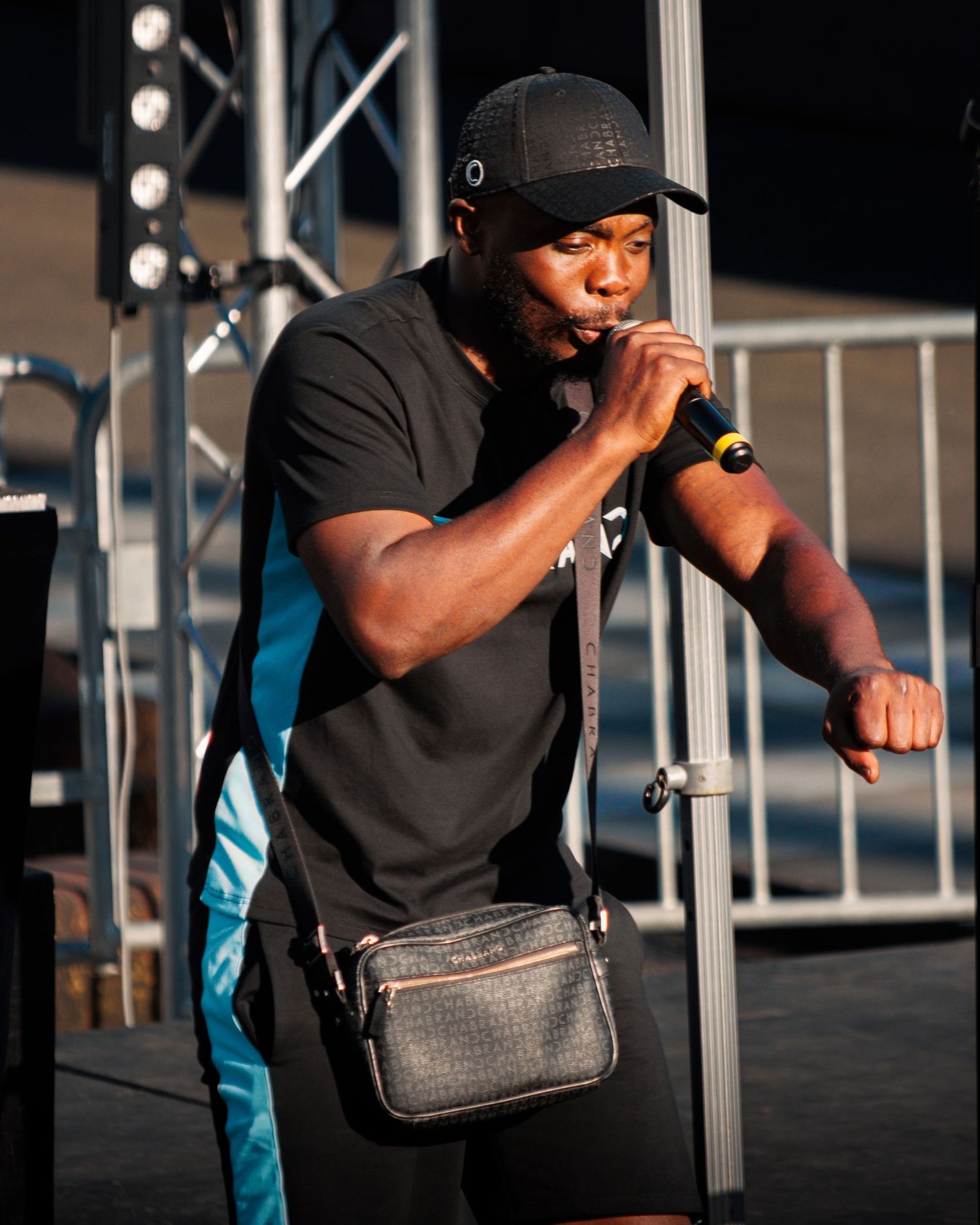 Performer in black attire holds microphone during outdoor performance.