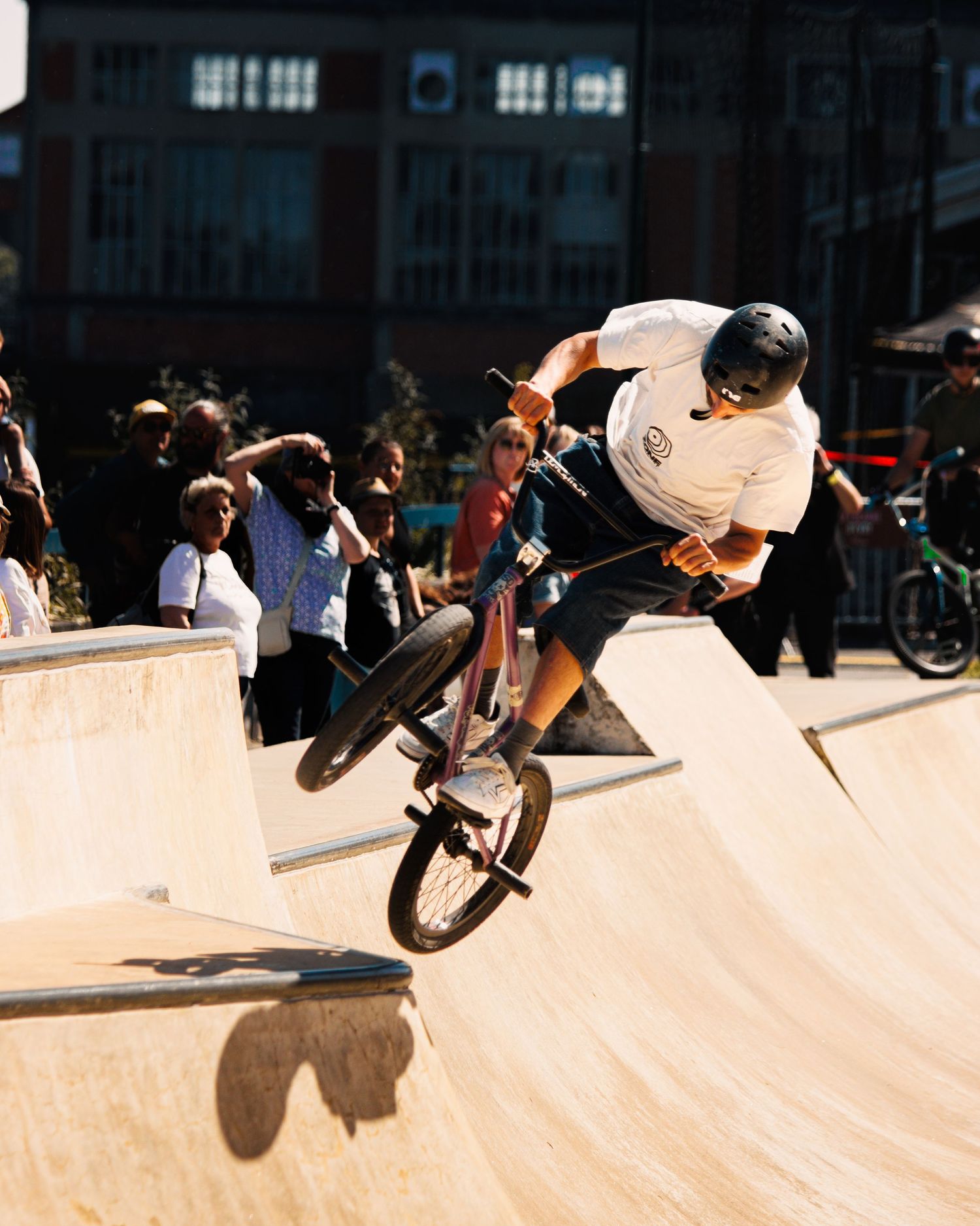 BMX rider executing aerial maneuver on skate park ramp with spectators watching.