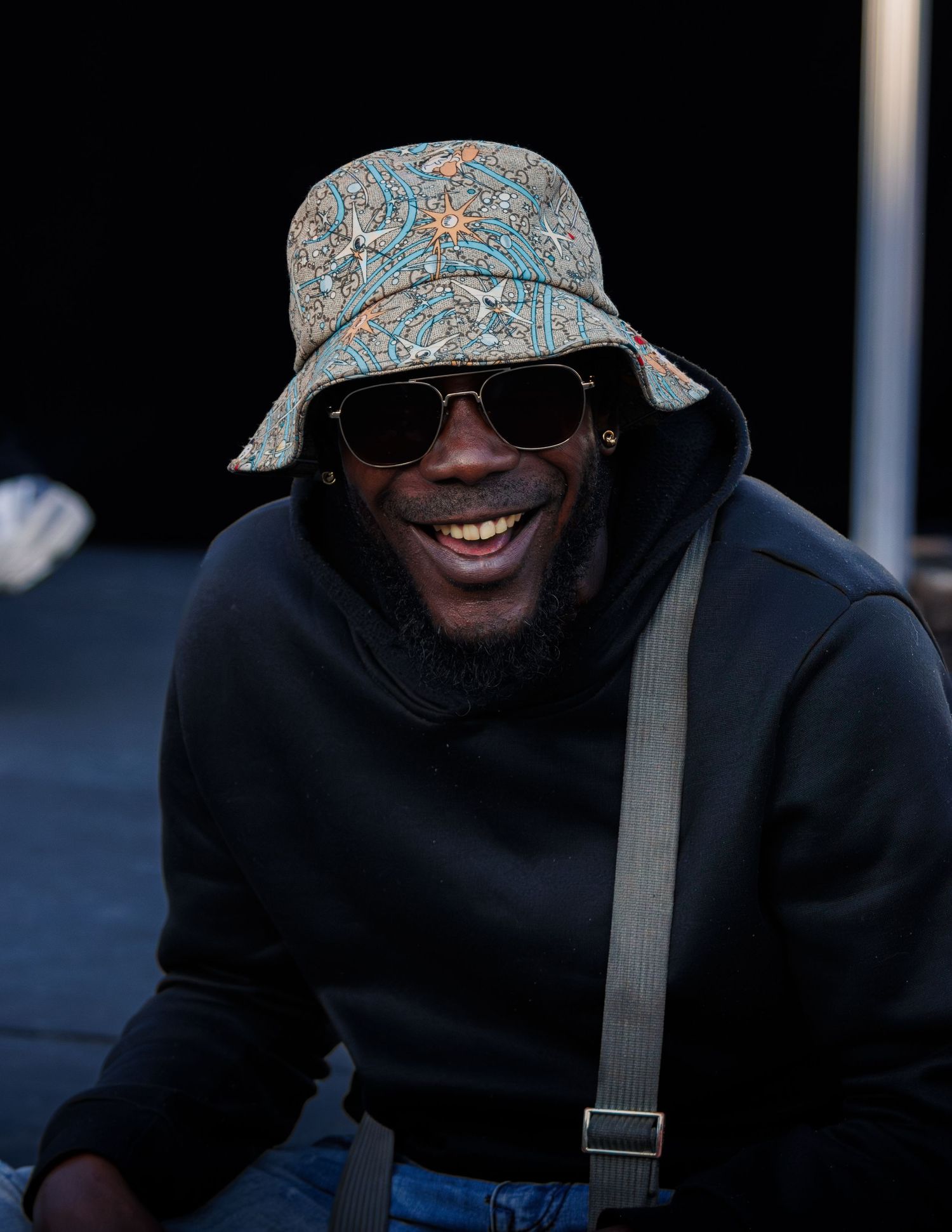 Person wearing floral bucket hat and sunglasses smiles brightly.