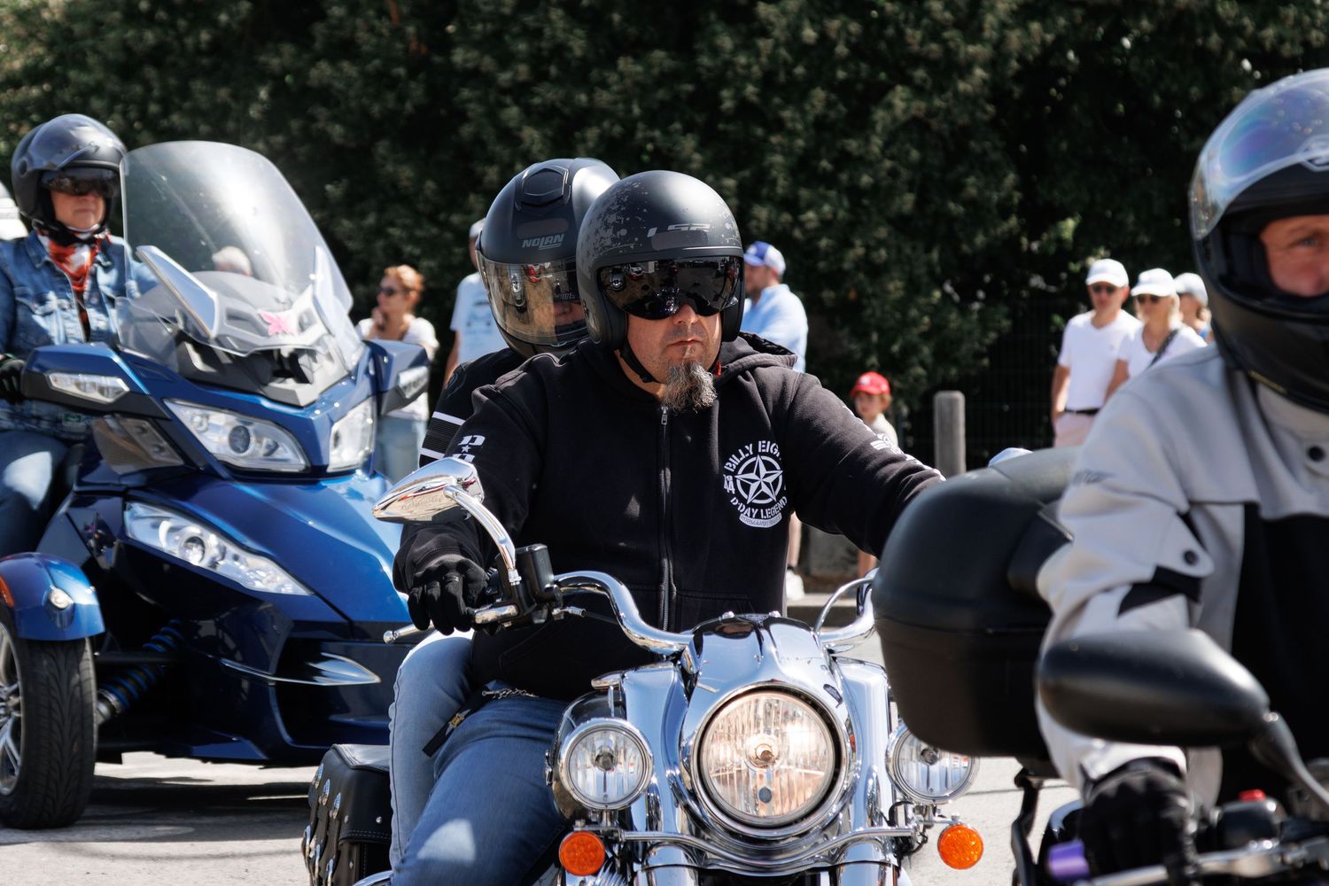 Group of motorcyclists wearing helmets riding motorcycles in a sunny outdoor event or parade.
