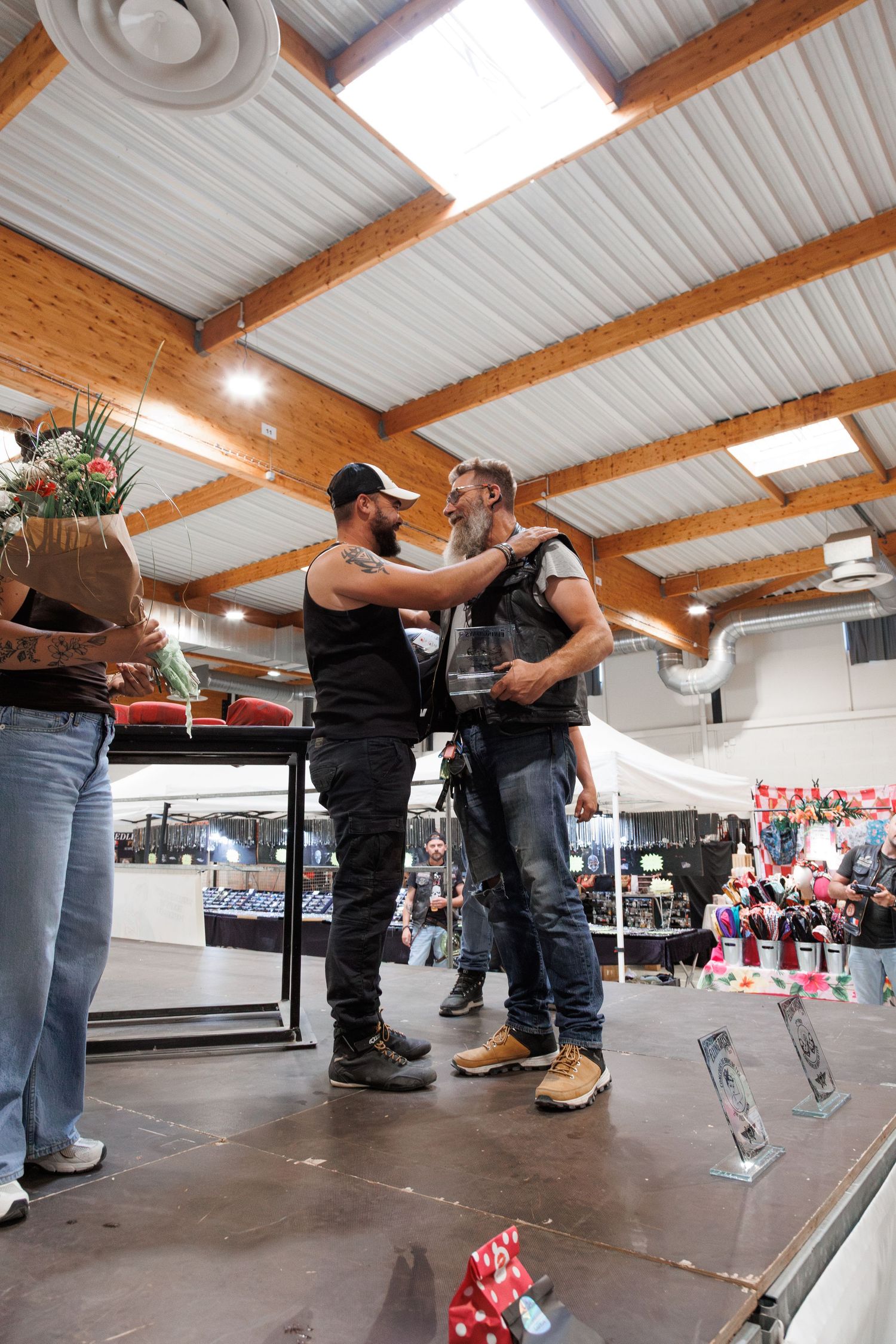 Two men sharing a moment on stage inside a rustic venue during an indoor event or award ceremony.