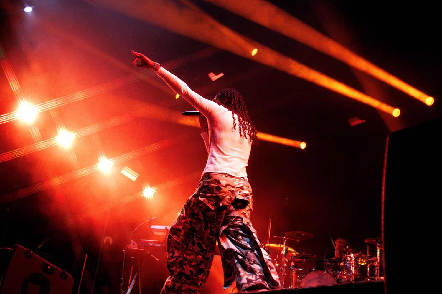 A performer on stage raises their fist under dramatic red and orange stage lights during a live concert.