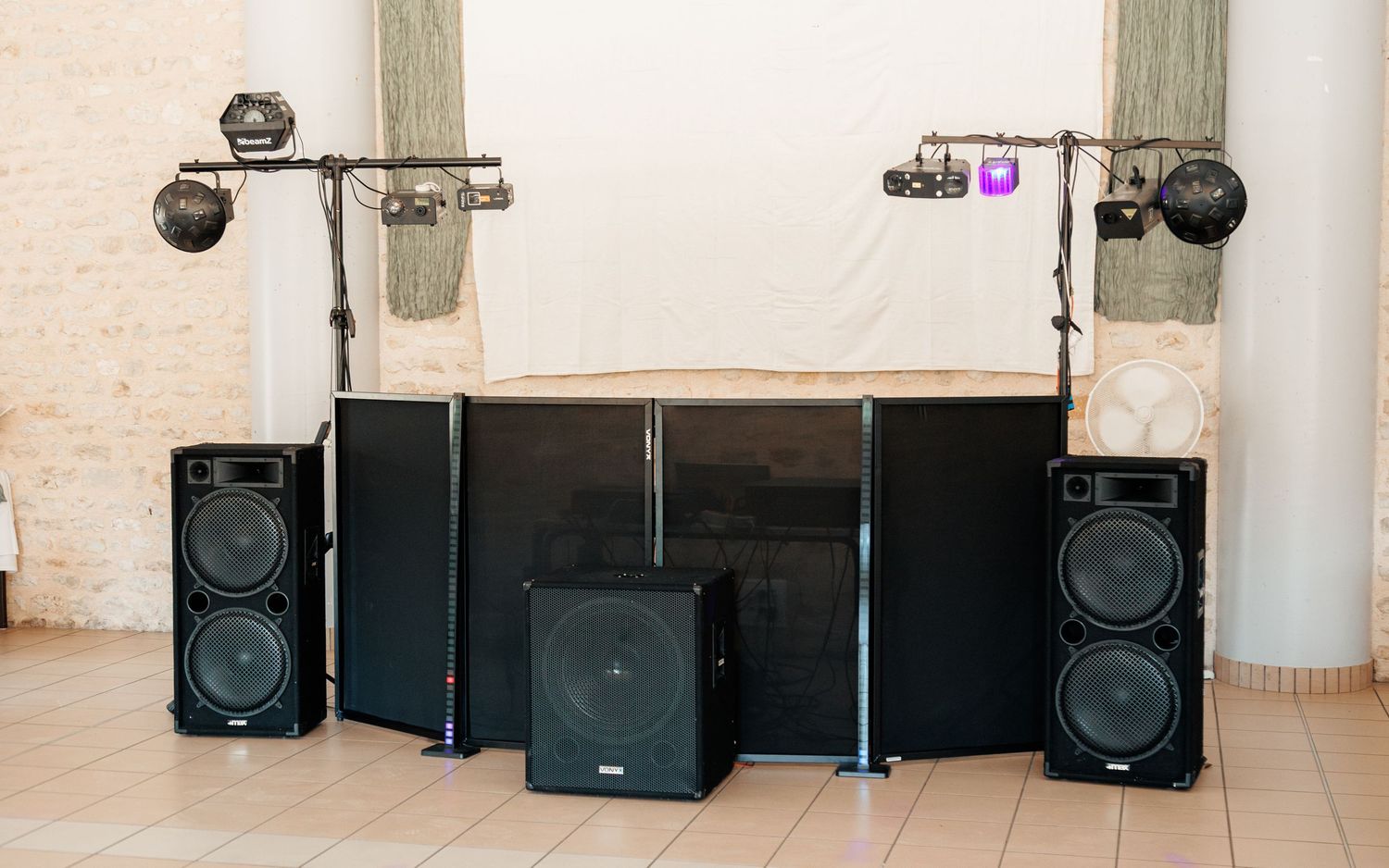 Professional DJ speaker setup with large black subwoofers and disco lights in stone venue hall.