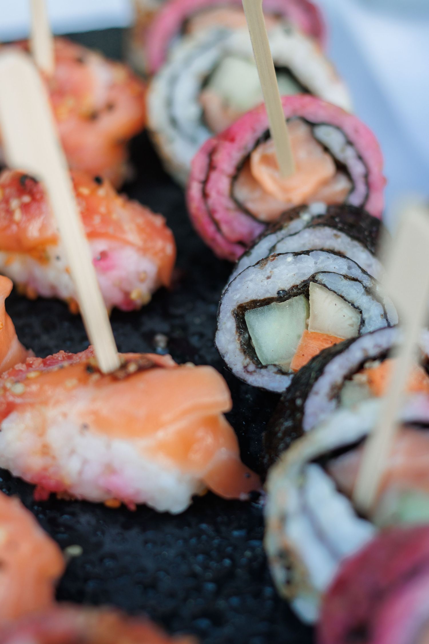 Close-up of assorted sushi rolls with toothpicks served on dark slate at wedding reception.